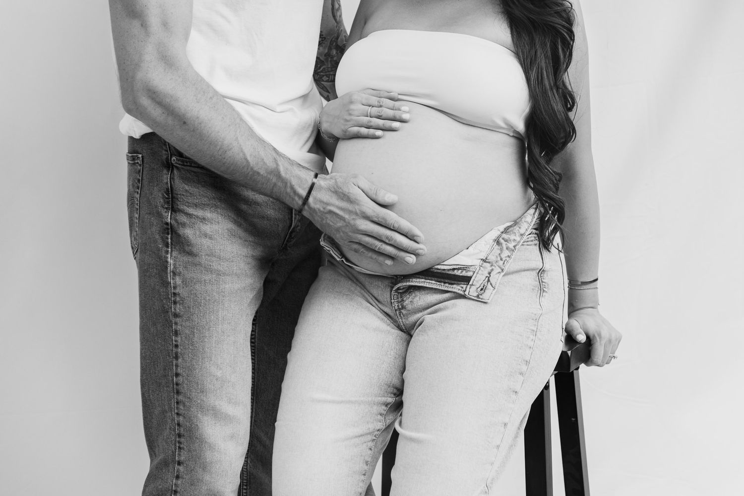 Black and white maternity photo showing couple embracing with hands on pregnant belly.