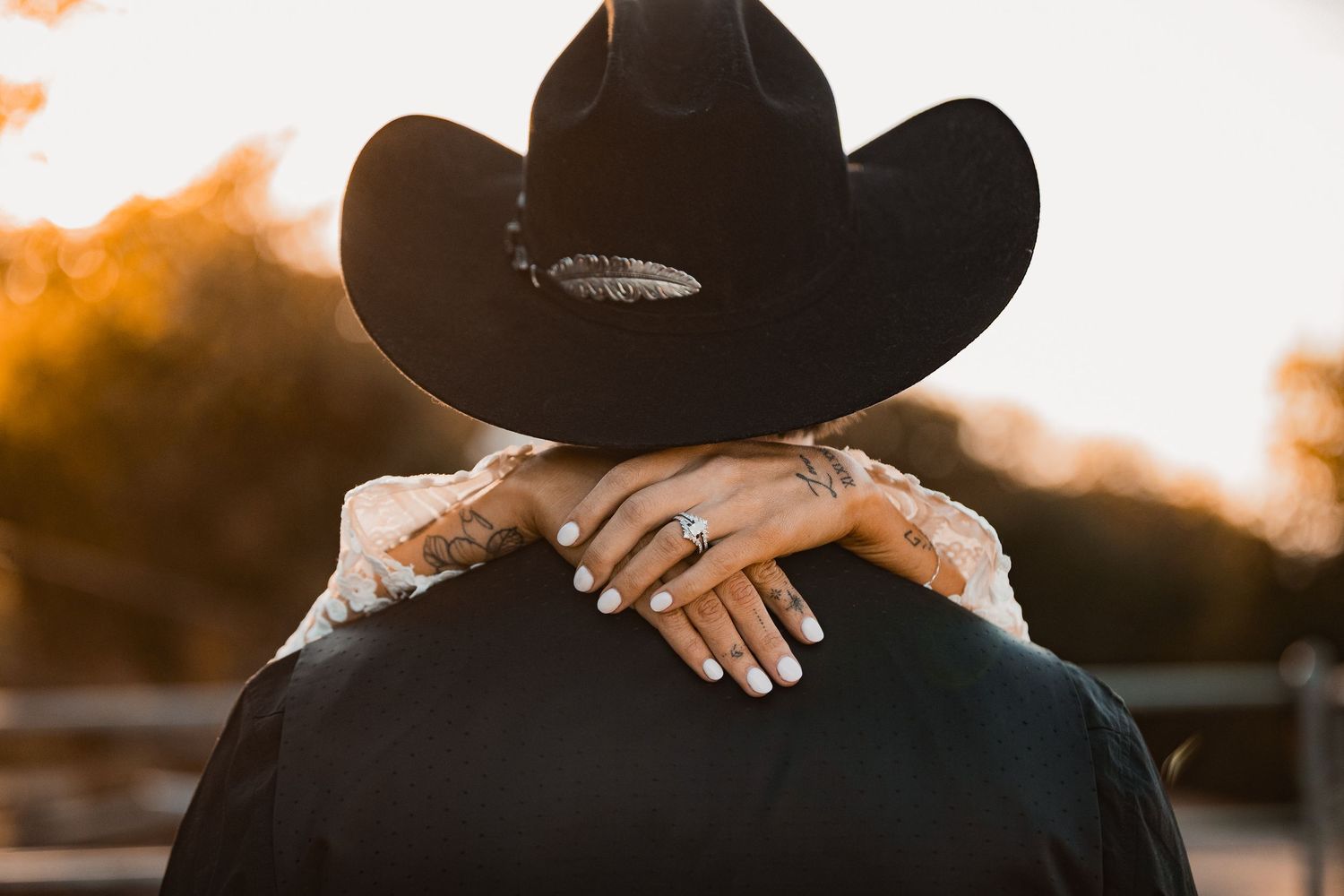 A silhouetted figure in a cowboy hat stands against a warm sunset backdrop with golden light filtering through.