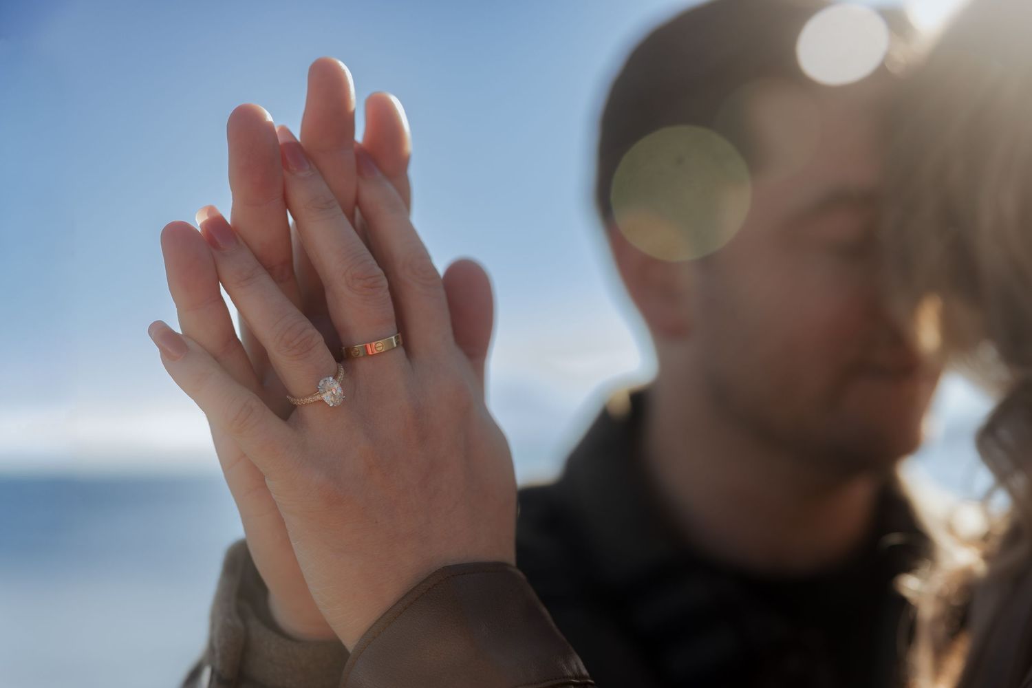 A series of hands with engagement rings photographed against a blurred outdoor background.