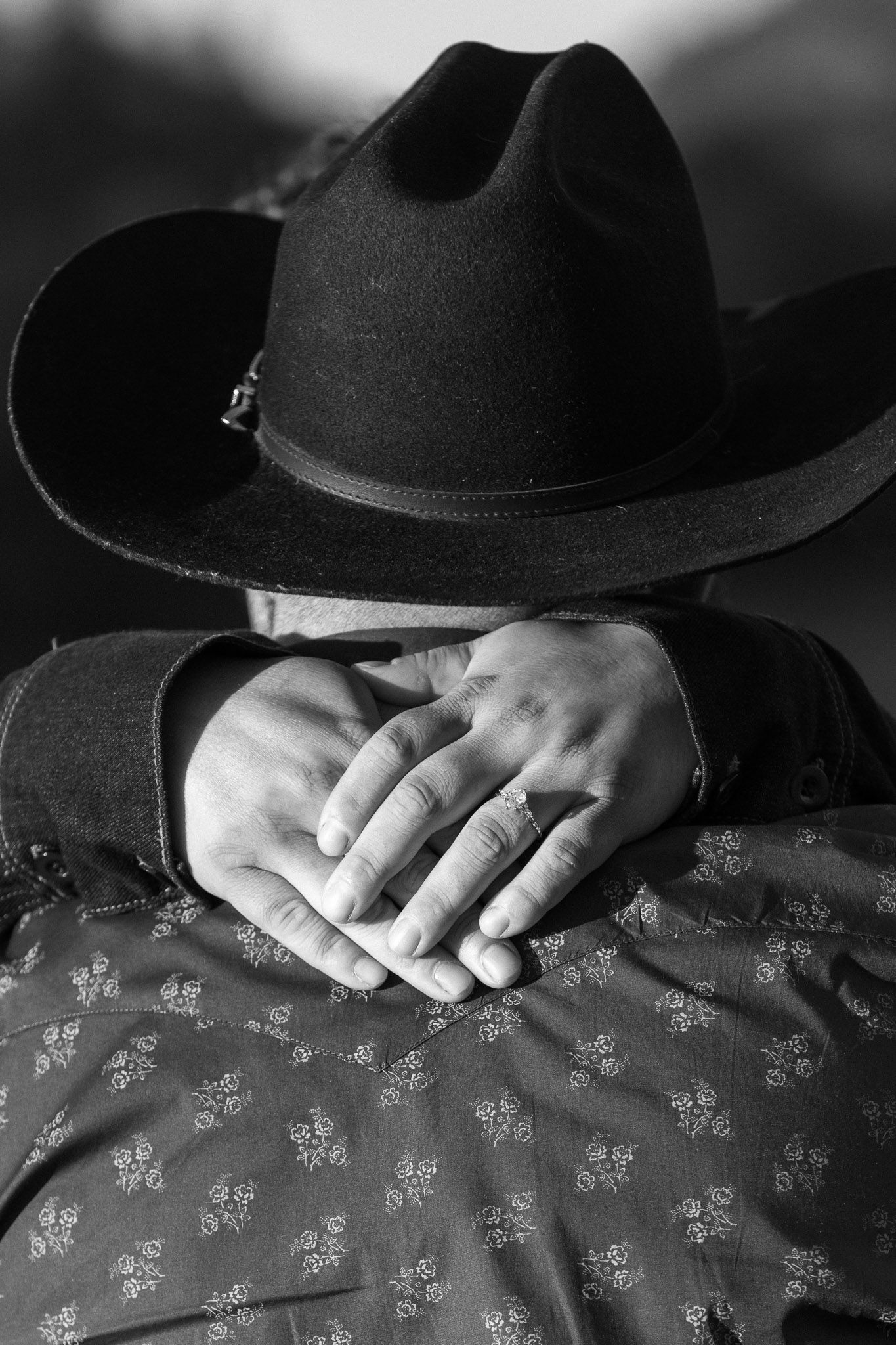 Black cowboy hat and folded hands on floral fabric in monochrome.