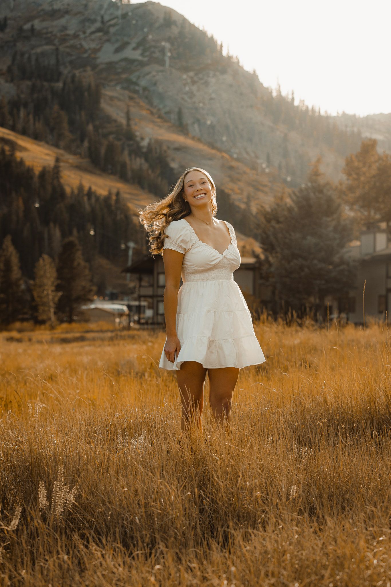 Person in white dress standing in mountain meadow during golden hour.