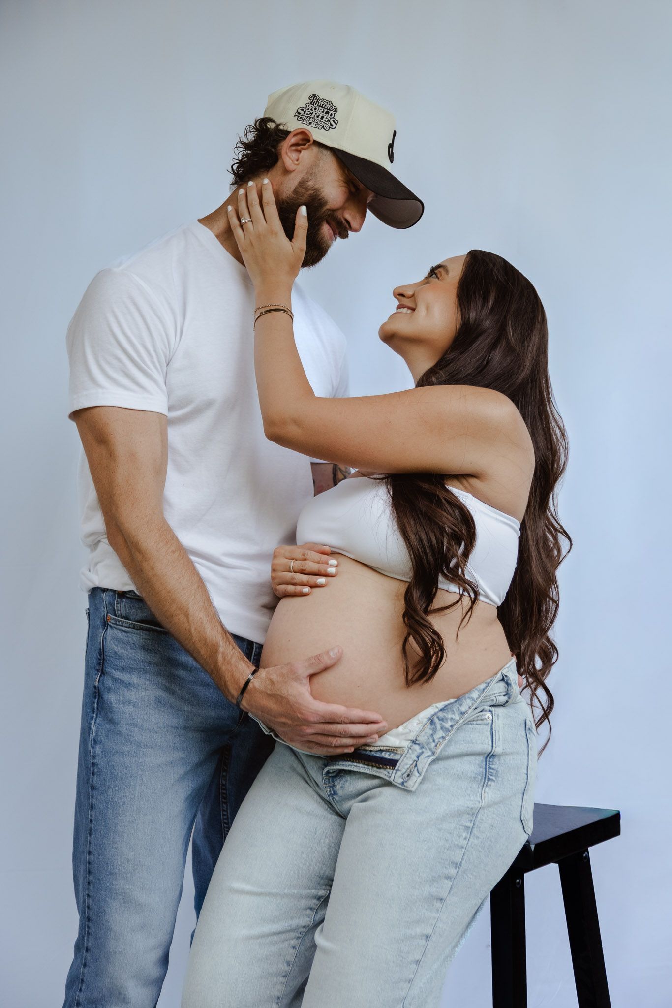 Couple in casual white and denim outfits embracing intimately against white background in romantic photoshoot series.