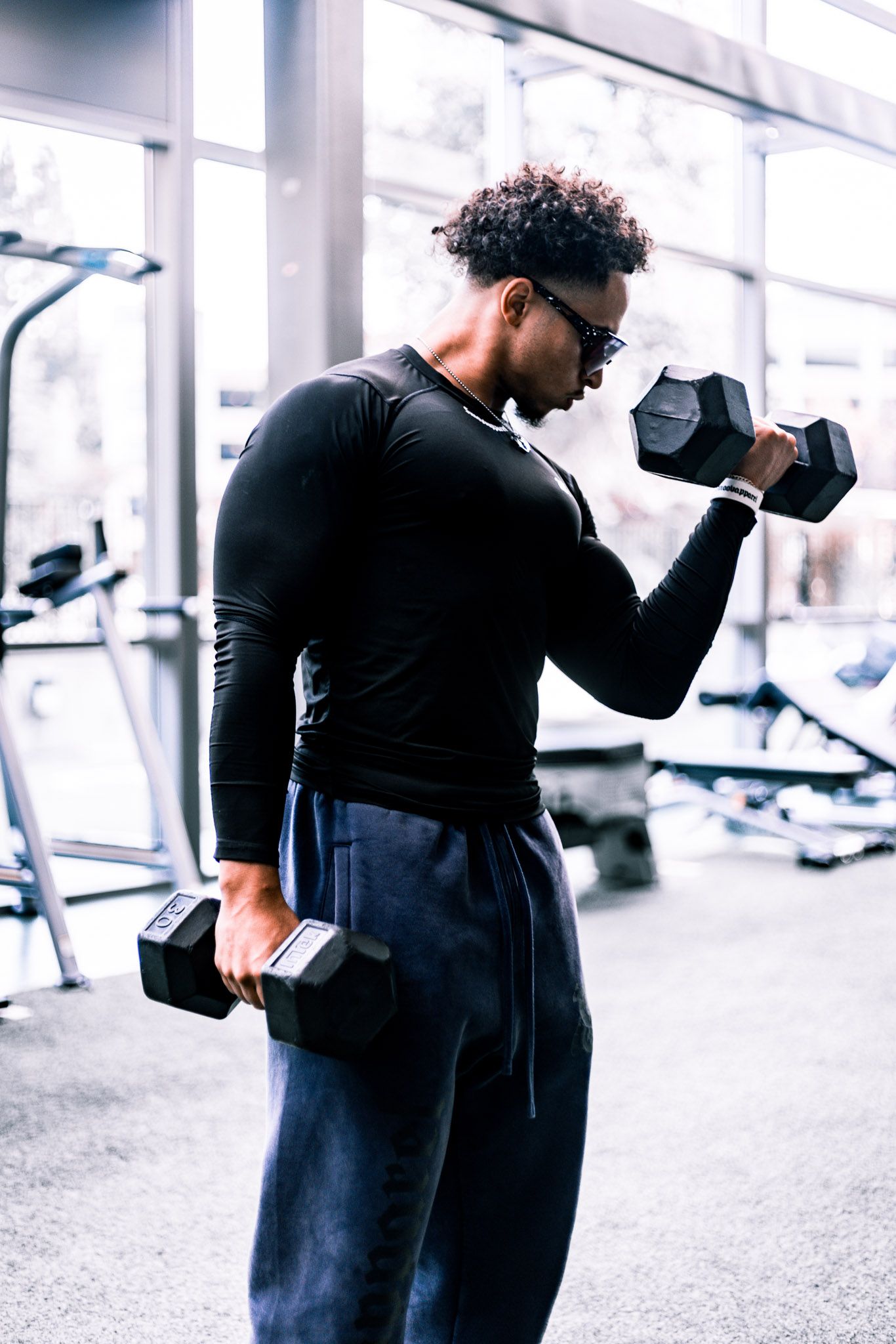 Person in black workout attire lifting dumbbells at a modern gym.
