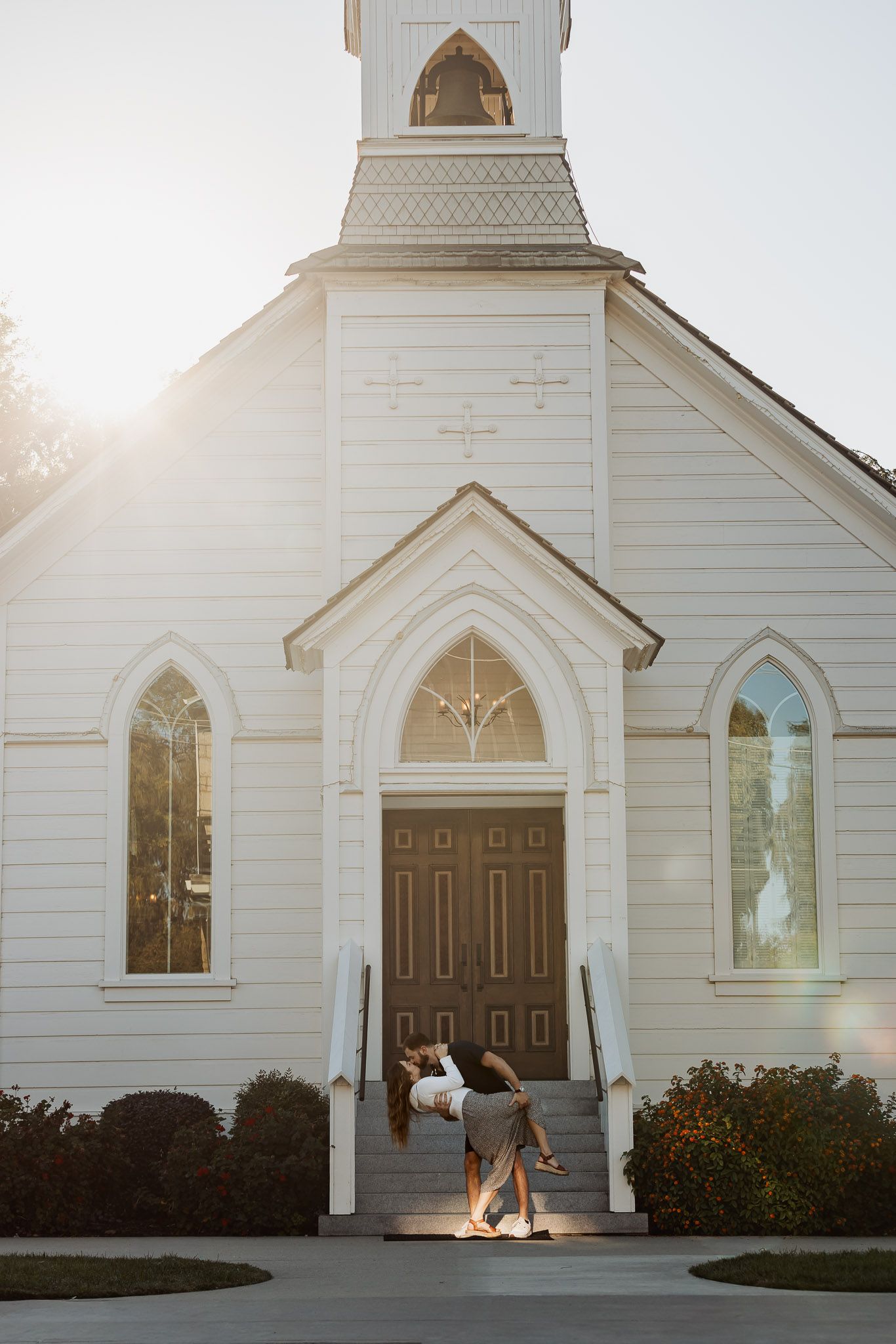 White country church exterior with sunlight streaming through steeple and arched windows.