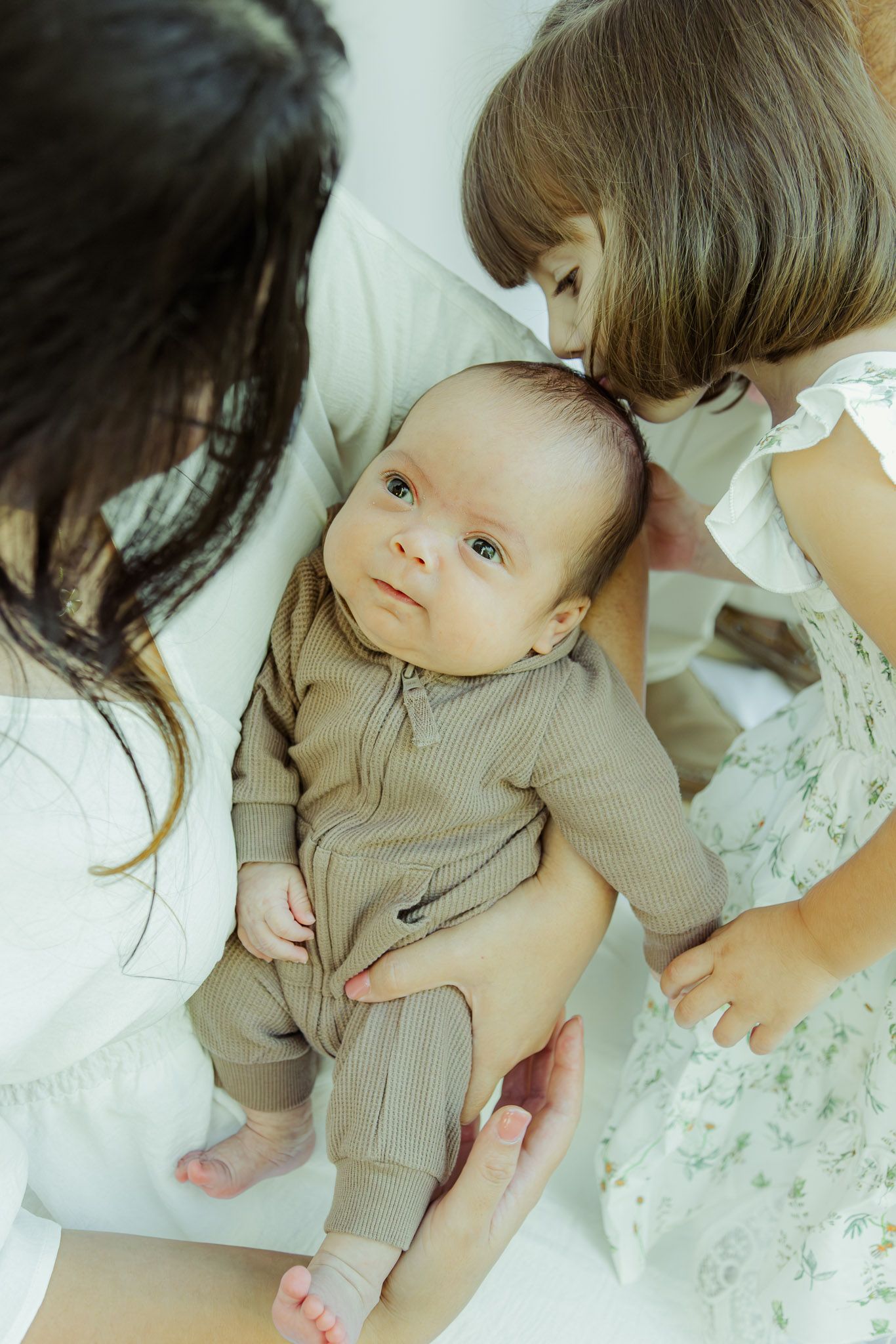 A series of tender moments showing a baby in a beige outfit lying on white floral bedding.