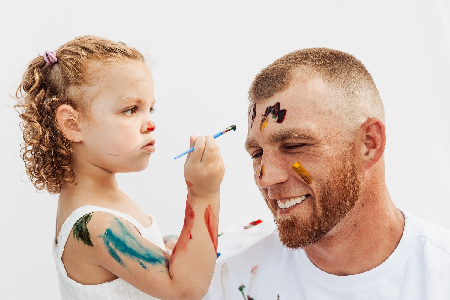 Child and adult having fun painting faces with colorful makeup.