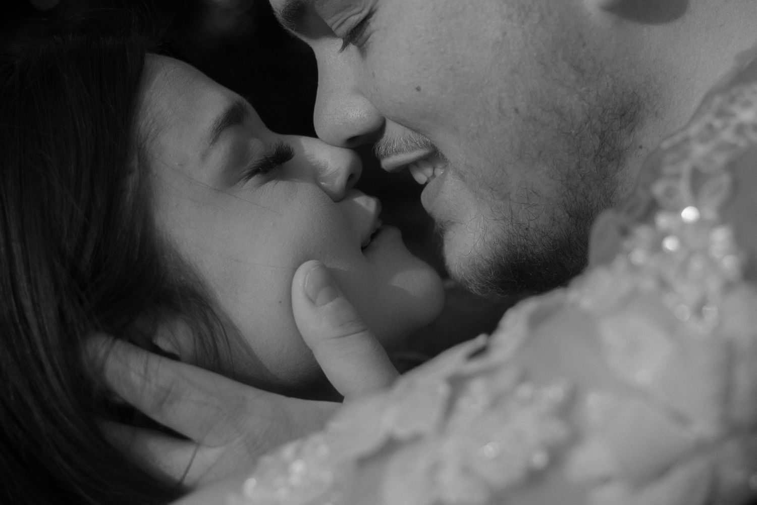 Black and white photo of a romantic couple almost kissing, bride in lace dress, intimate wedding moment.
