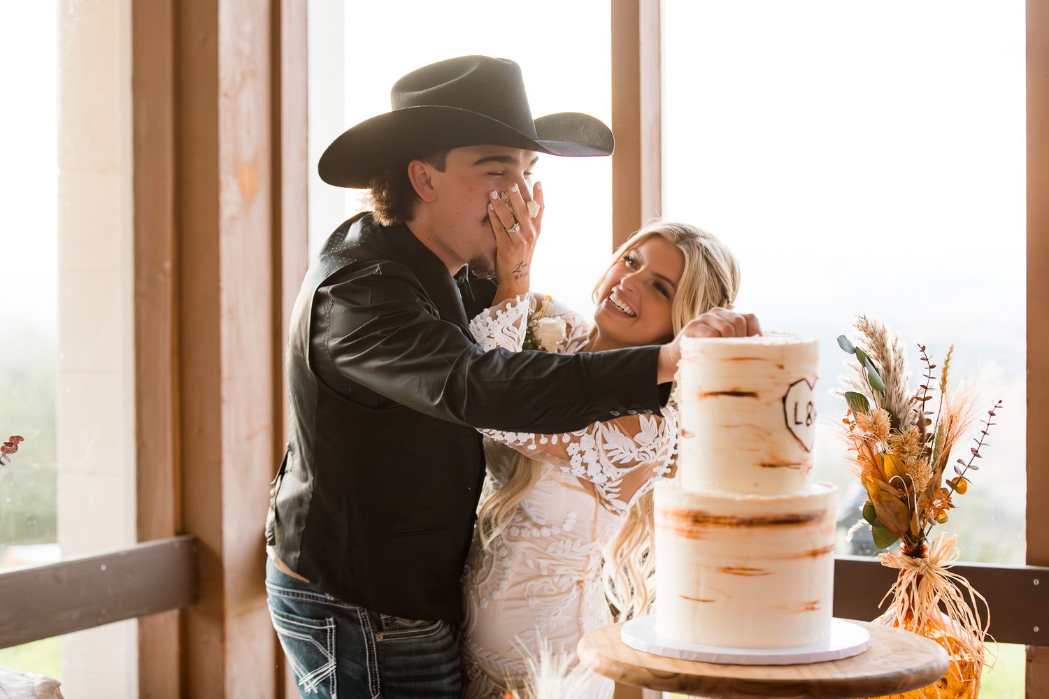 Newlyweds share a playful cake-cutting moment at their rustic western wedding reception.