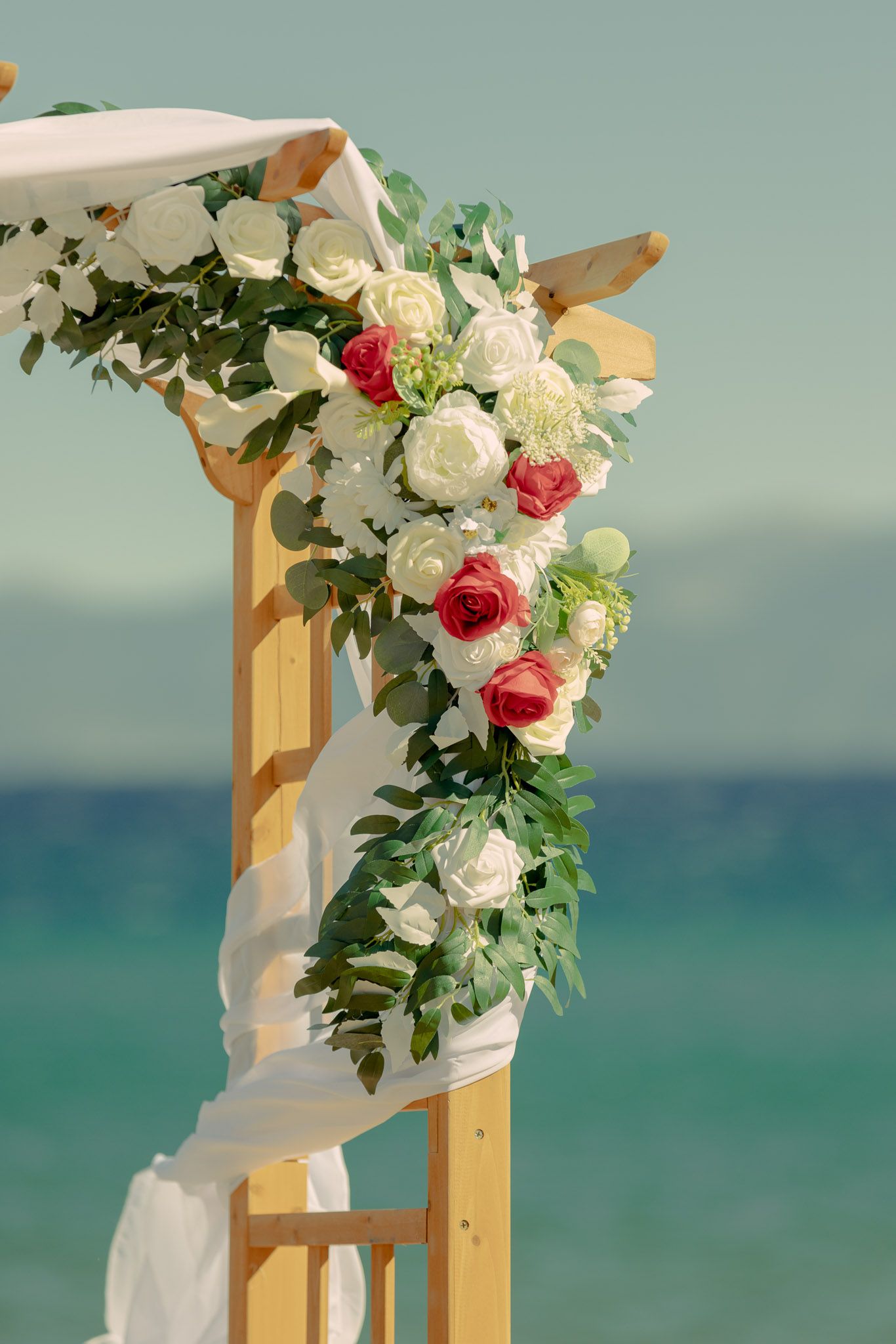 Beach wedding arch decorated with white and pink roses against turquoise ocean backdrop.