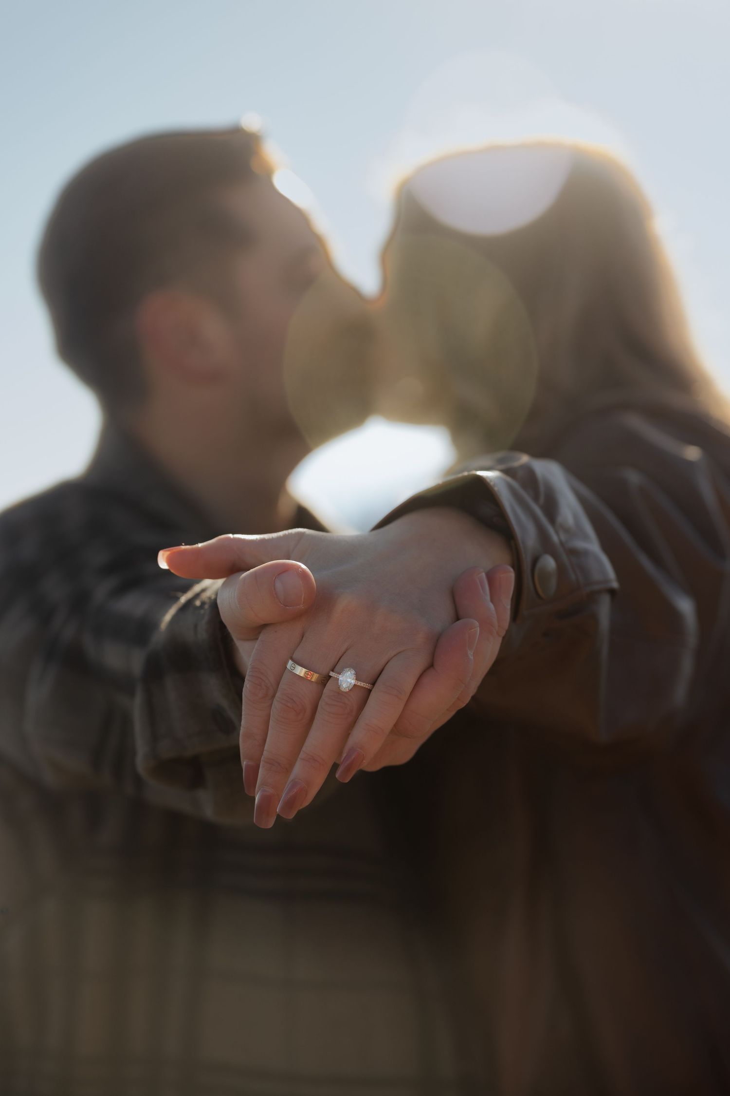 A hand with a ring is silhouetted against a soft, blurred background during sunset.