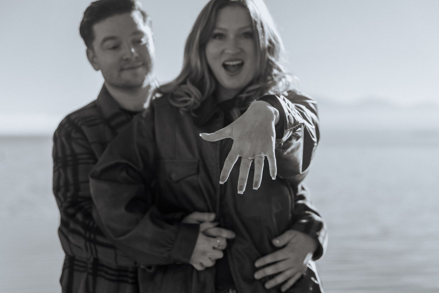 A couple embraces and laughs together against a bright outdoor background.