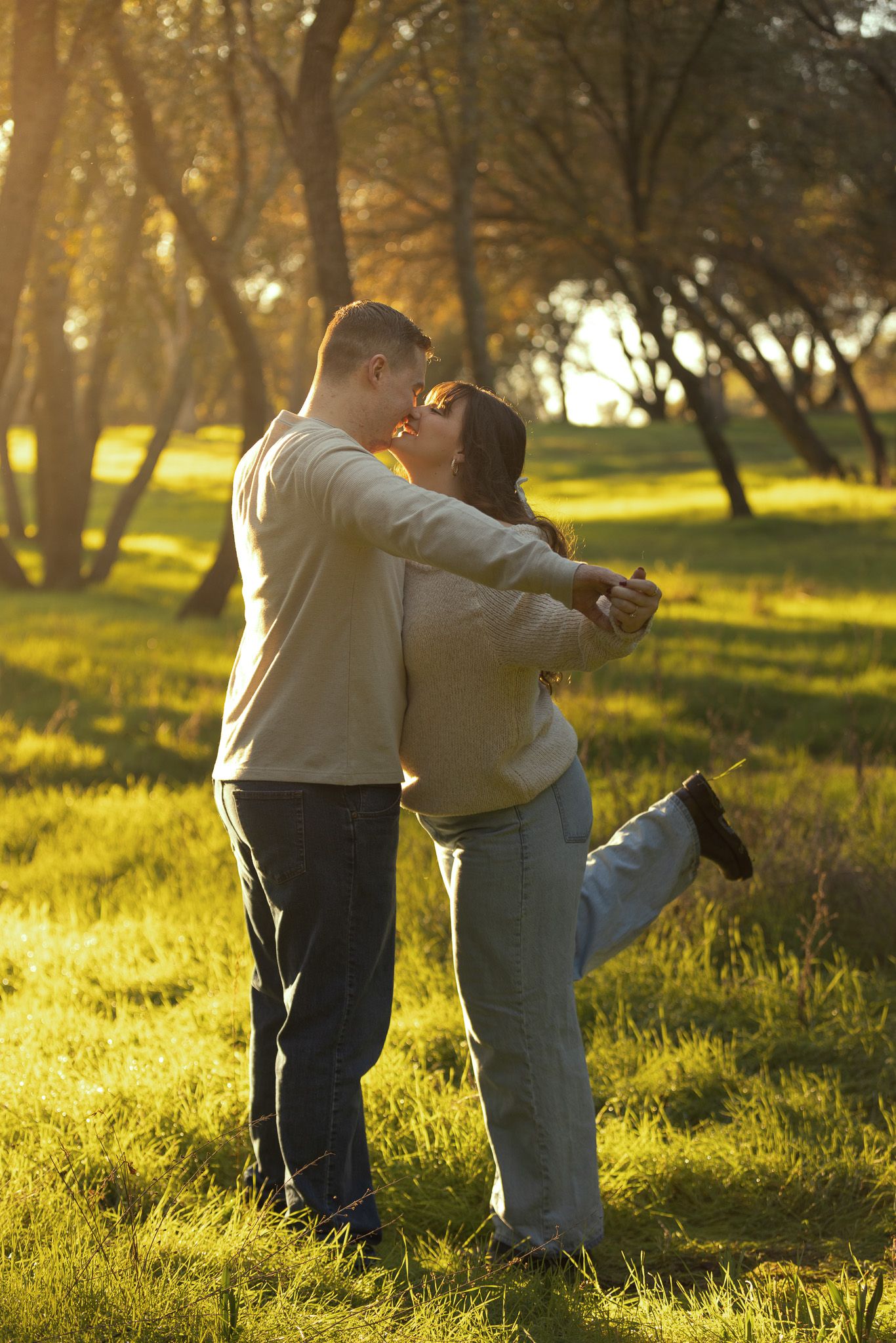 A couple embraces in a sunlit park during golden hour as warm light filters through autumn trees.