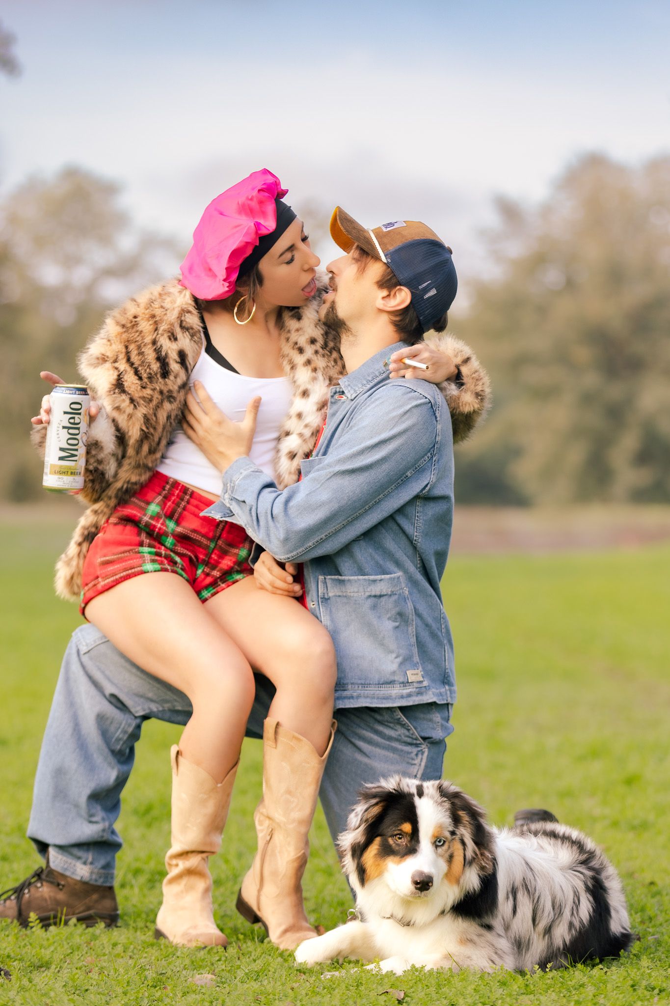 A couple shares a romantic moment in a grassy field with their Australian Shepherd dog resting beside them.