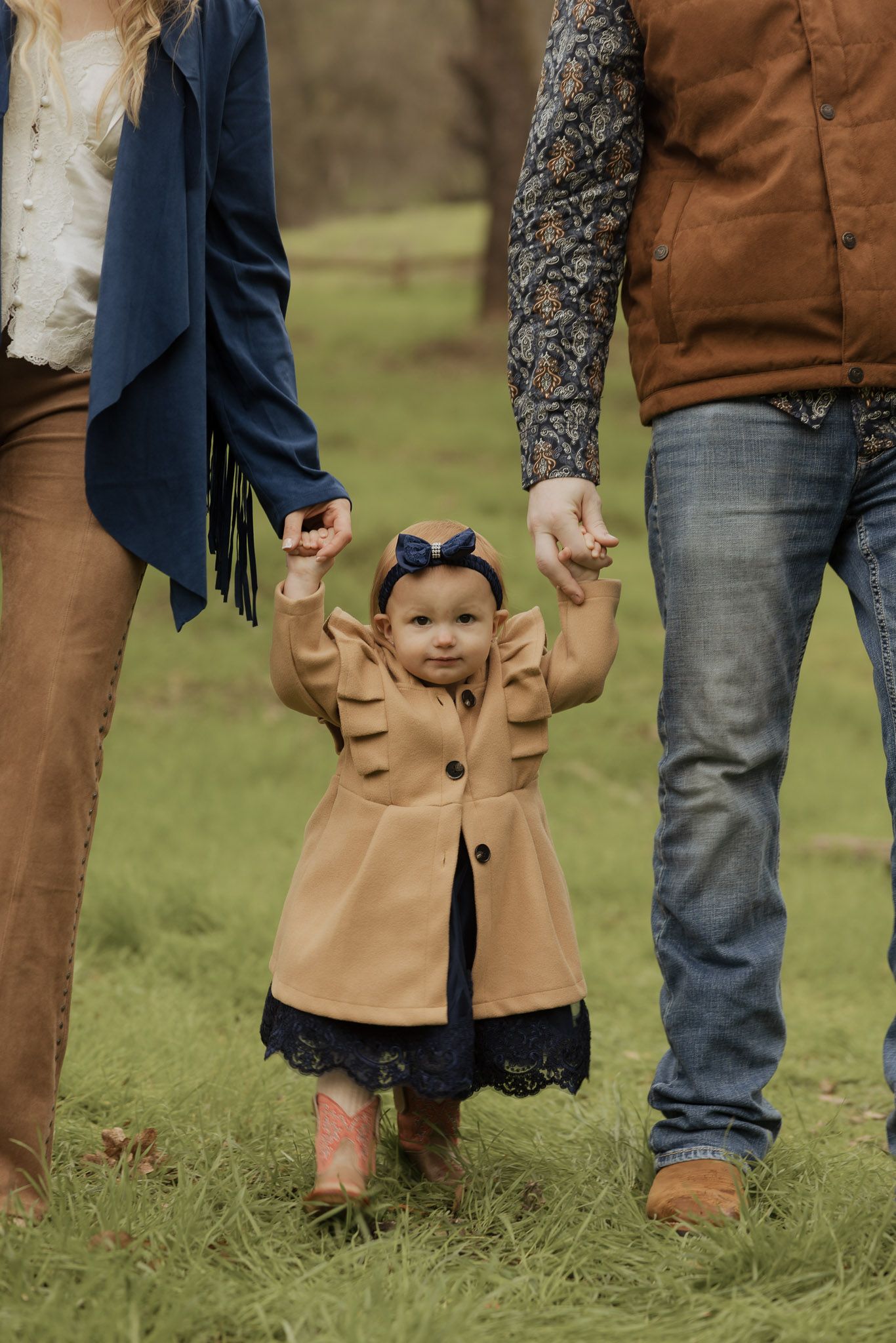 Cropped view of family members' legs and feet standing together on grass wearing jeans and brown boots.