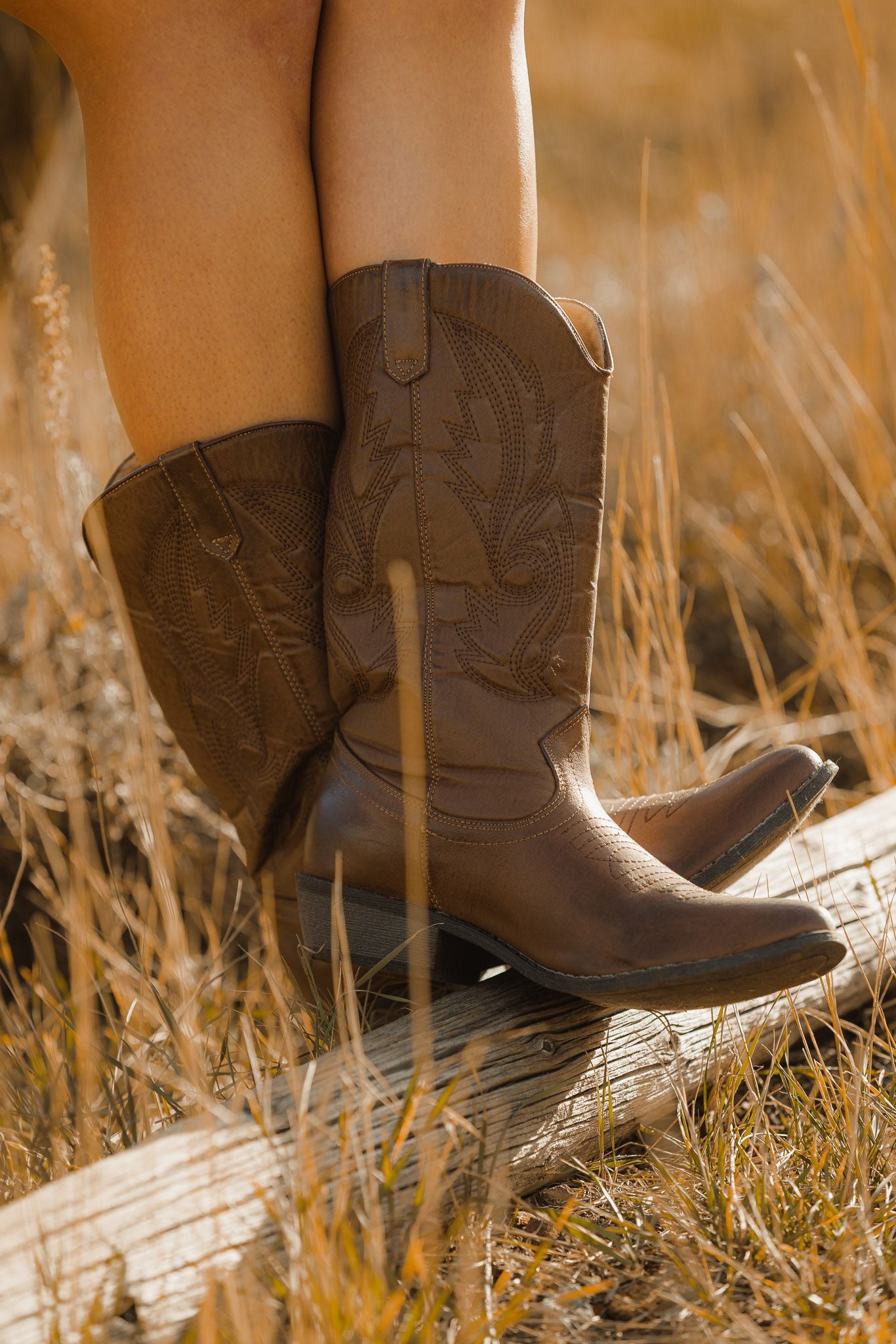 Brown leather cowboy boots in tall golden grass during sunset.
