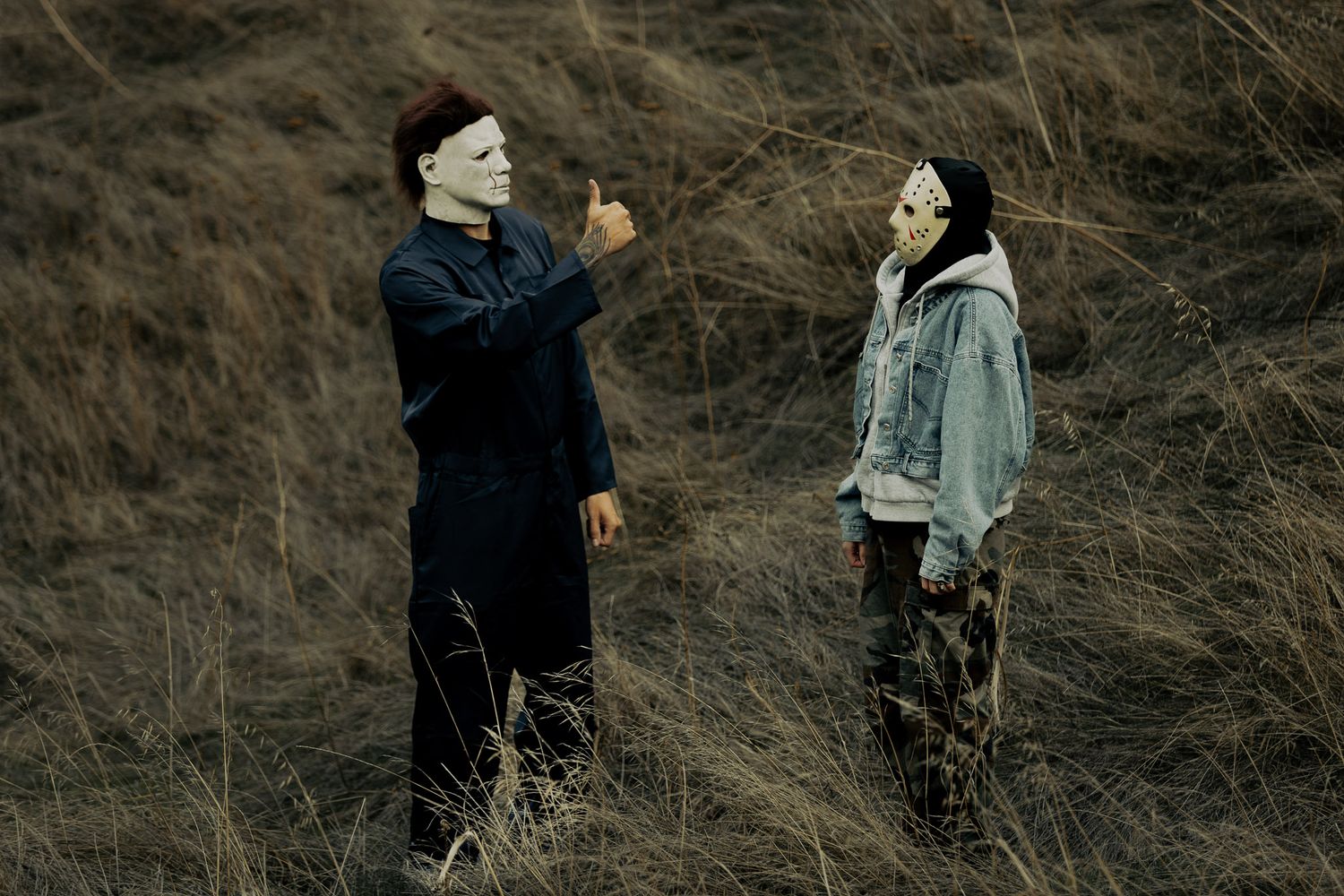 Two people walking through dry grass and brush on a hillside in casual clothing.