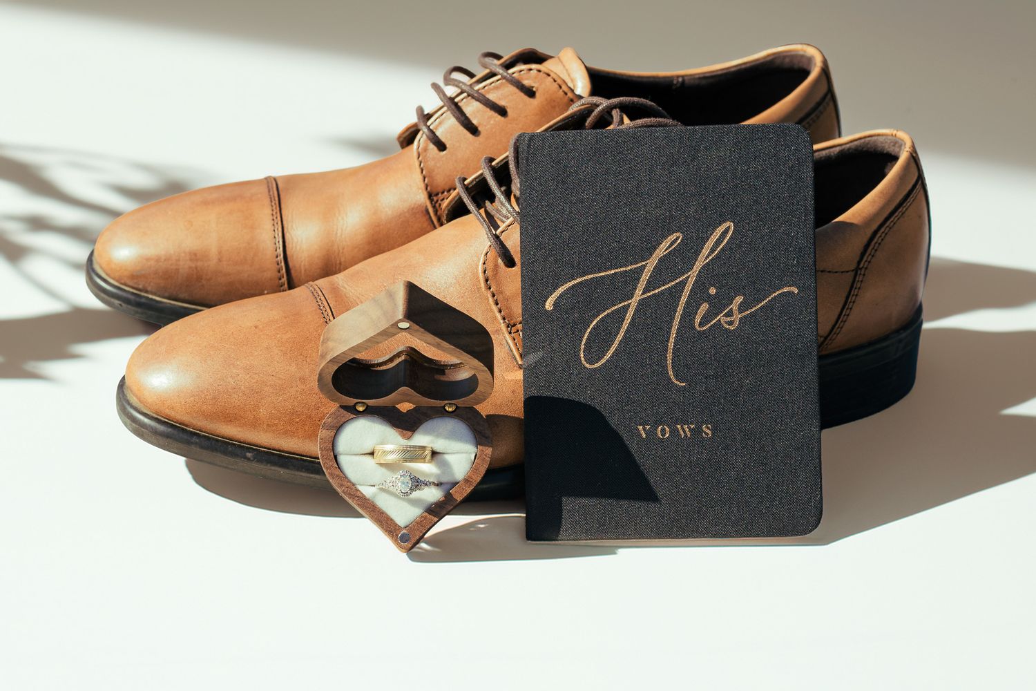 Brown leather dress shoes with wedding stationery in dramatic lighting.