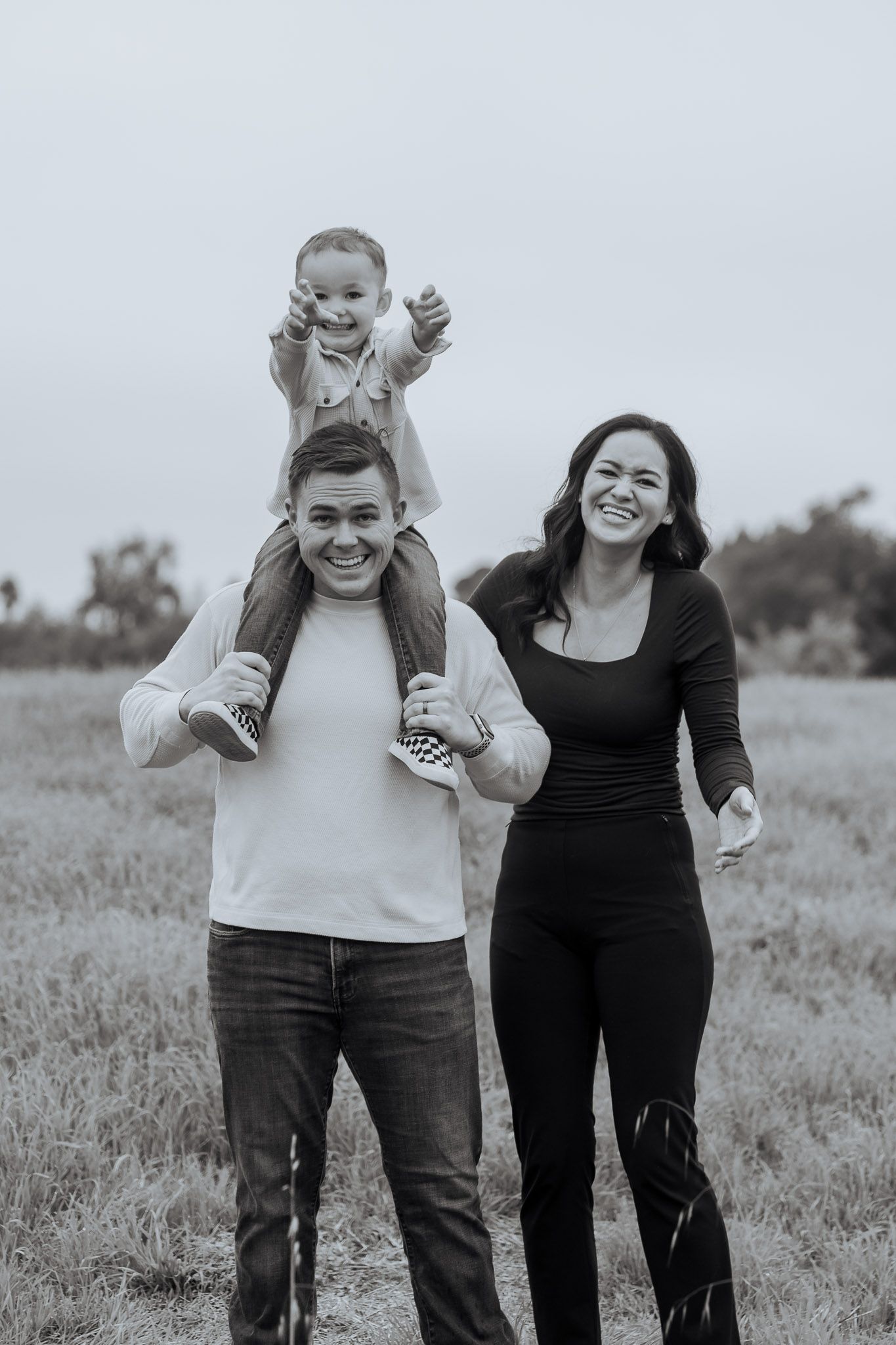A joyful family shares candid moments together in a field during a black and white photo session.