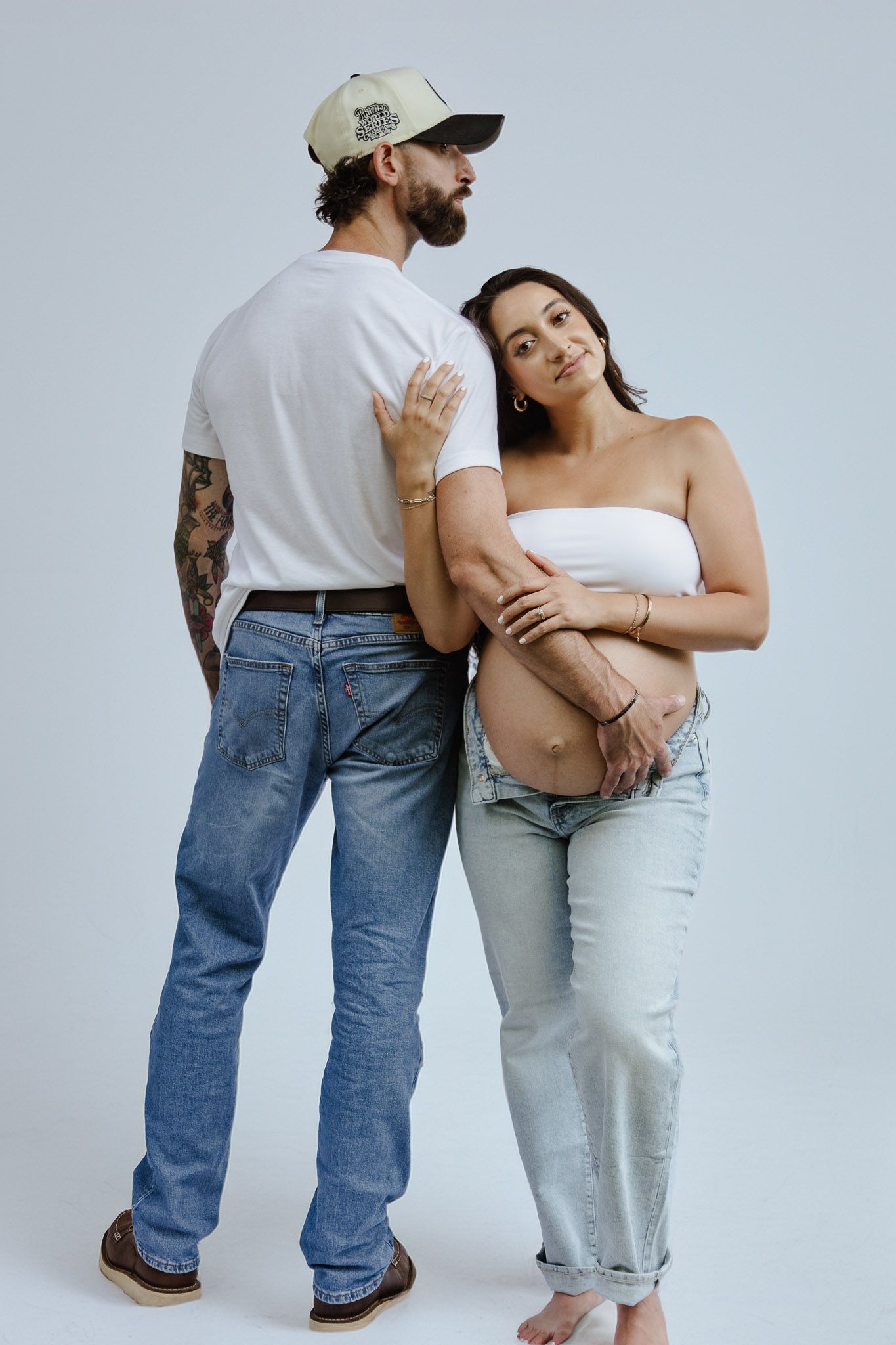 Couple poses together in casual denim and white attire against a studio background.