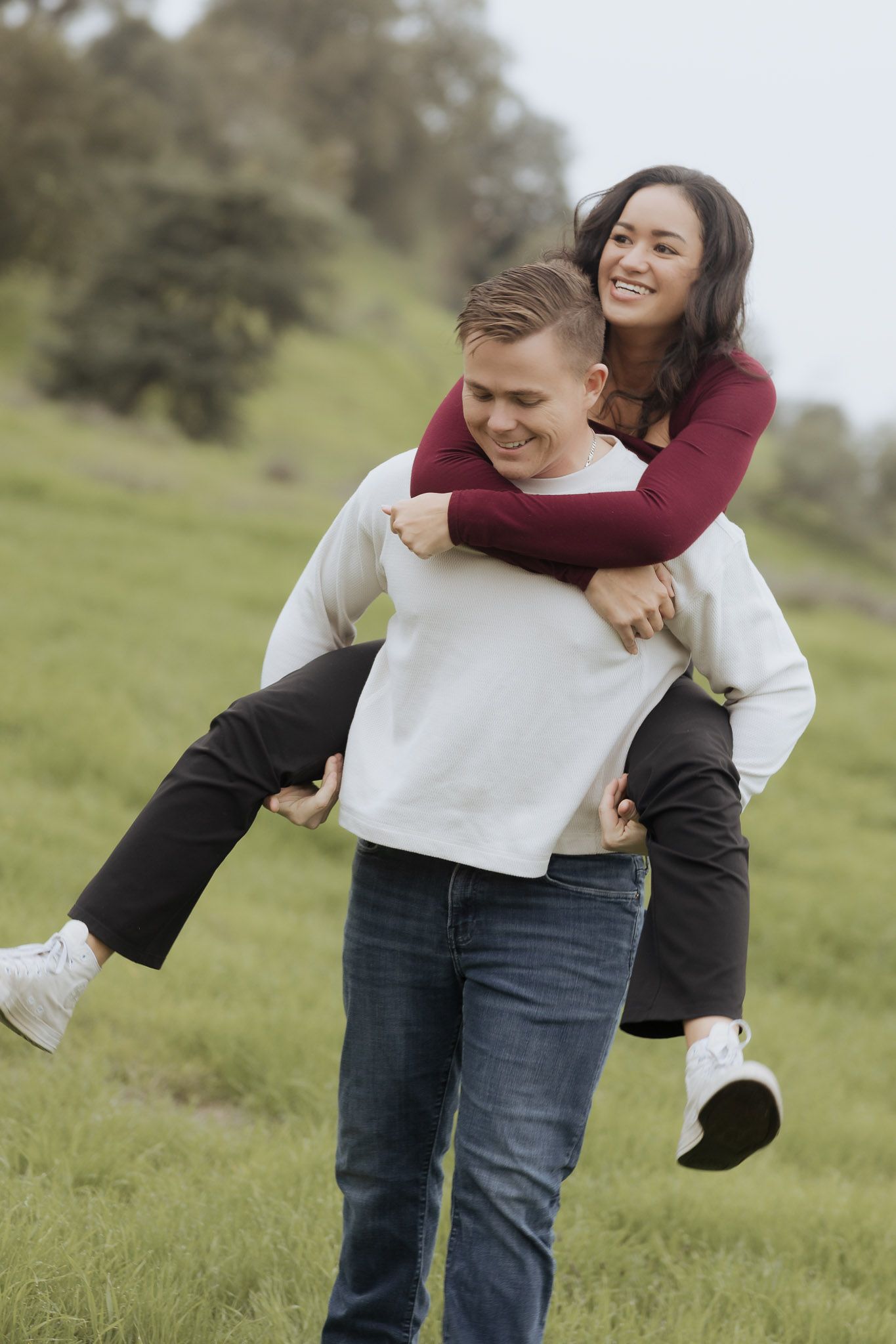 Couple enjoying piggyback ride in grassy field on sunny day.
