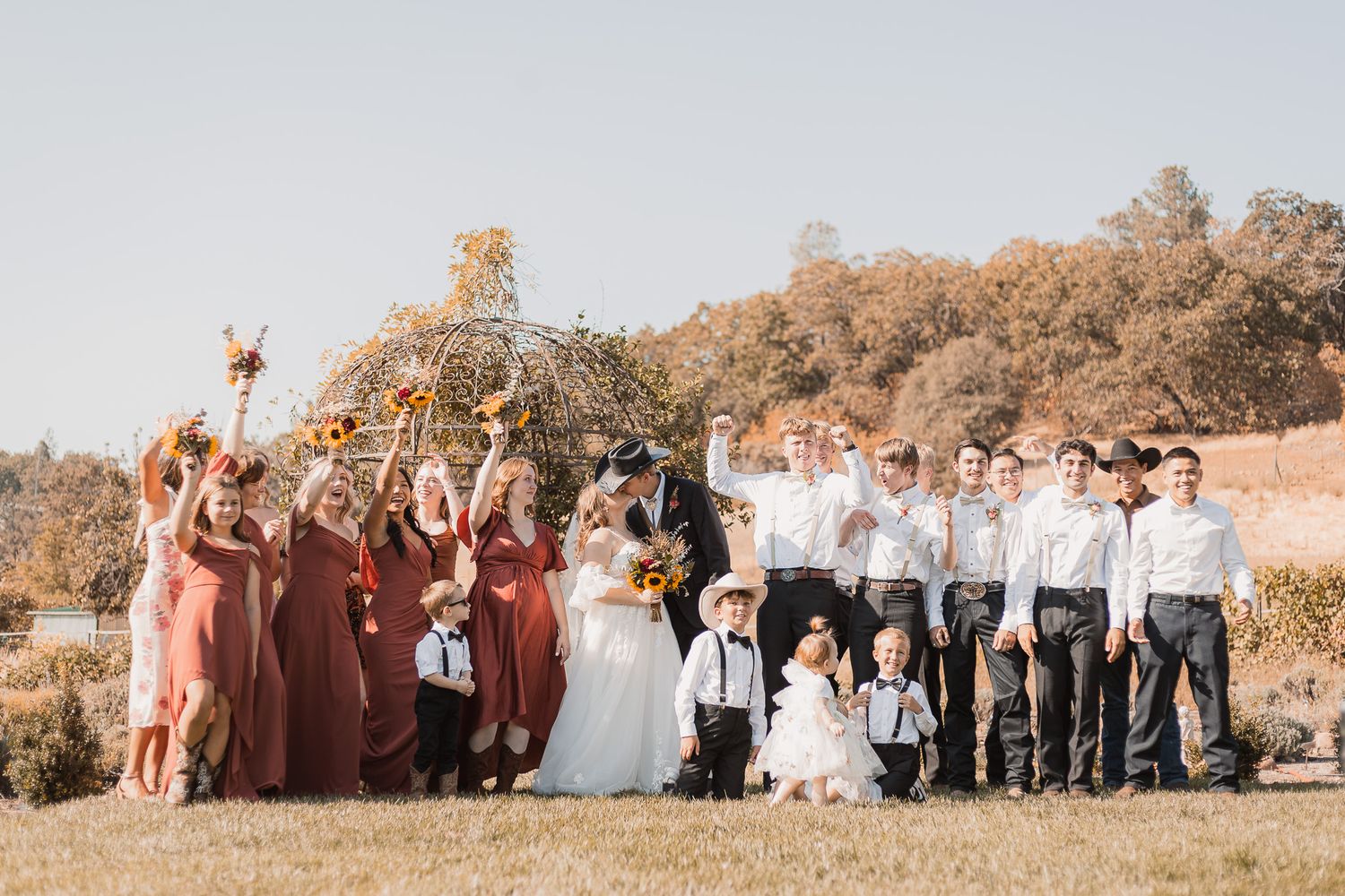 Large wedding party group photo taken outdoors in warm autumn colors.