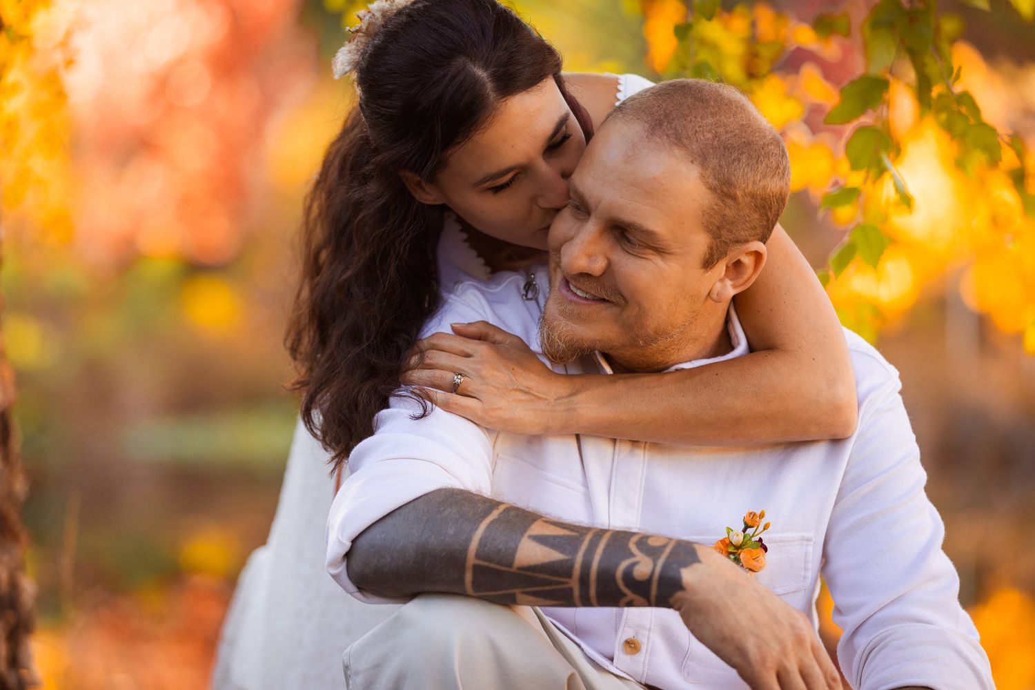 Couple embracing outdoors during golden hour with autumn foliage in background.