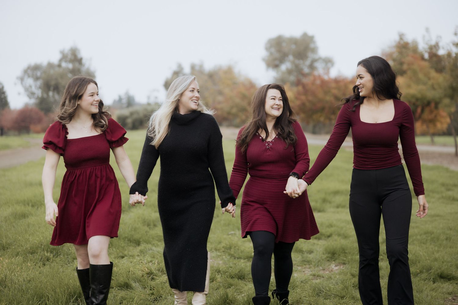 A group of people wearing burgundy and black outfits walk together through an autumn field.