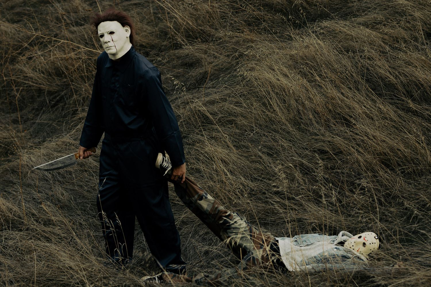 Dark silhouette figure stands against dry grass field in moody atmospheric horror scene.