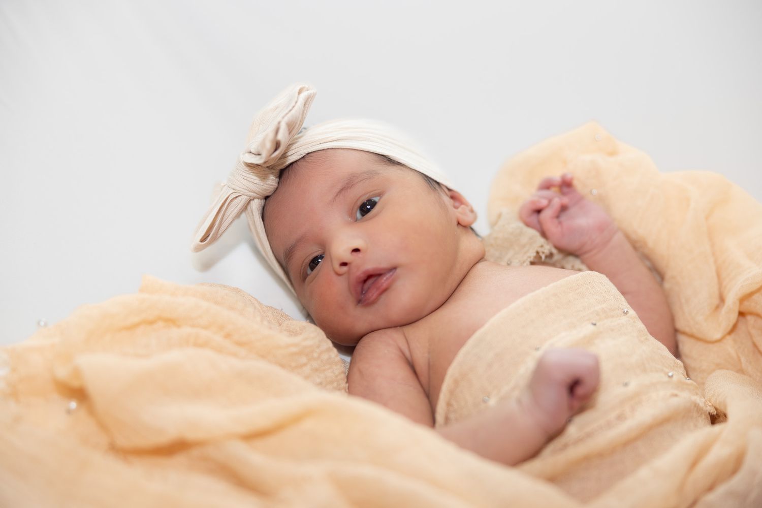 A newborn baby lies peacefully on a white blanket while being photographed from multiple angles.