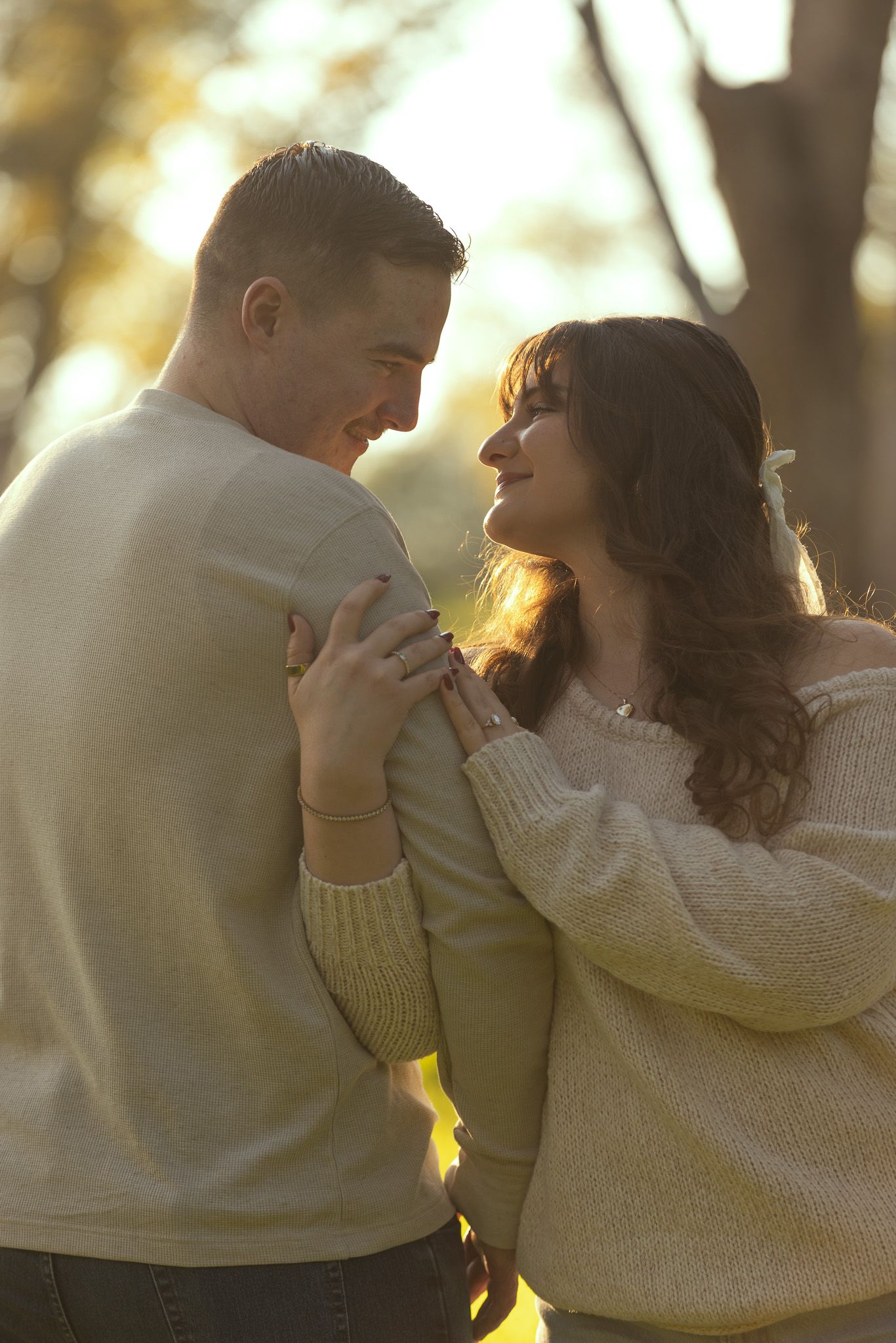 A romantic couple embraces in warm sunlight while wearing cozy cream-colored sweaters.