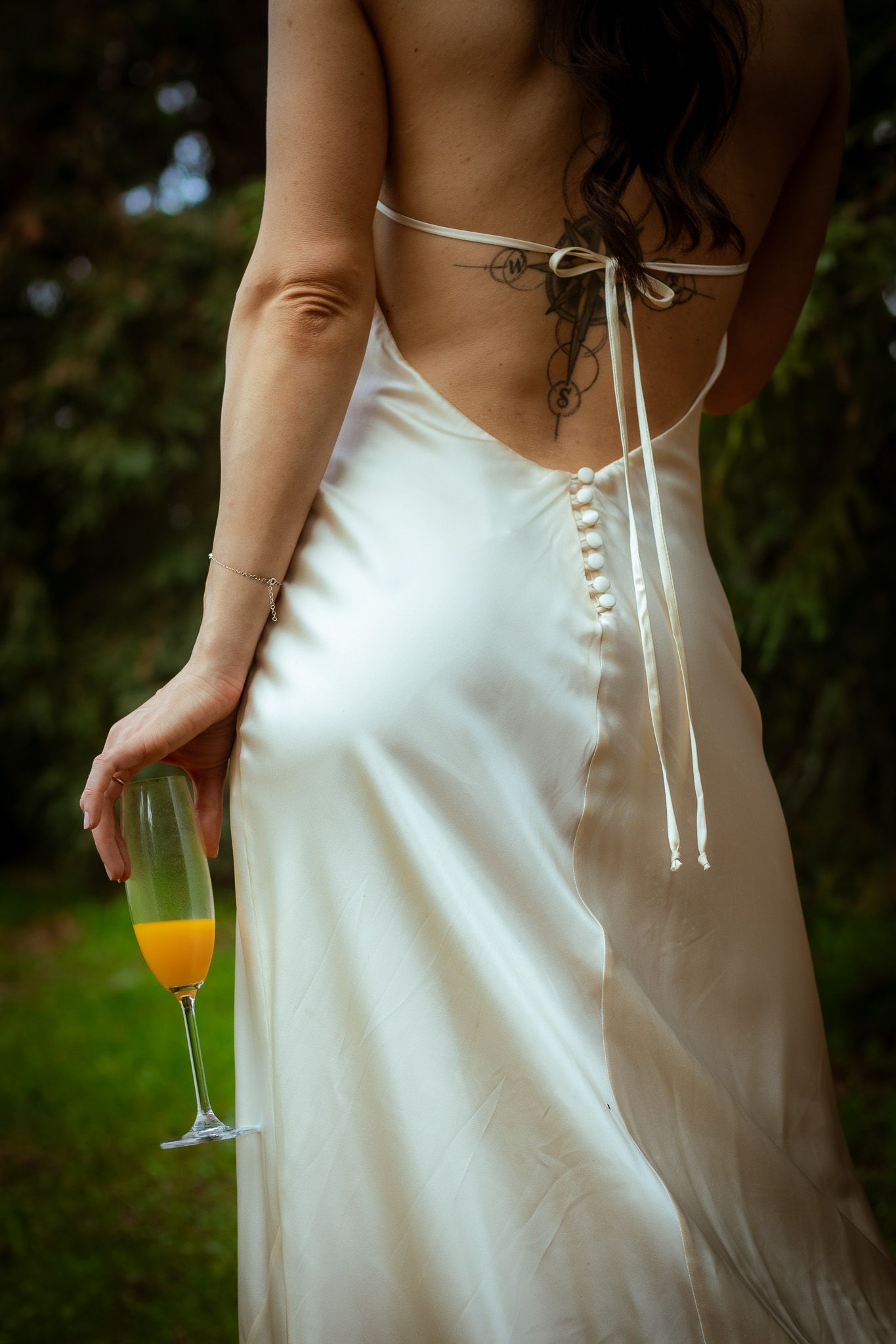 Back detail of white wedding dress with corset-style ribbon lacing and champagne glass.