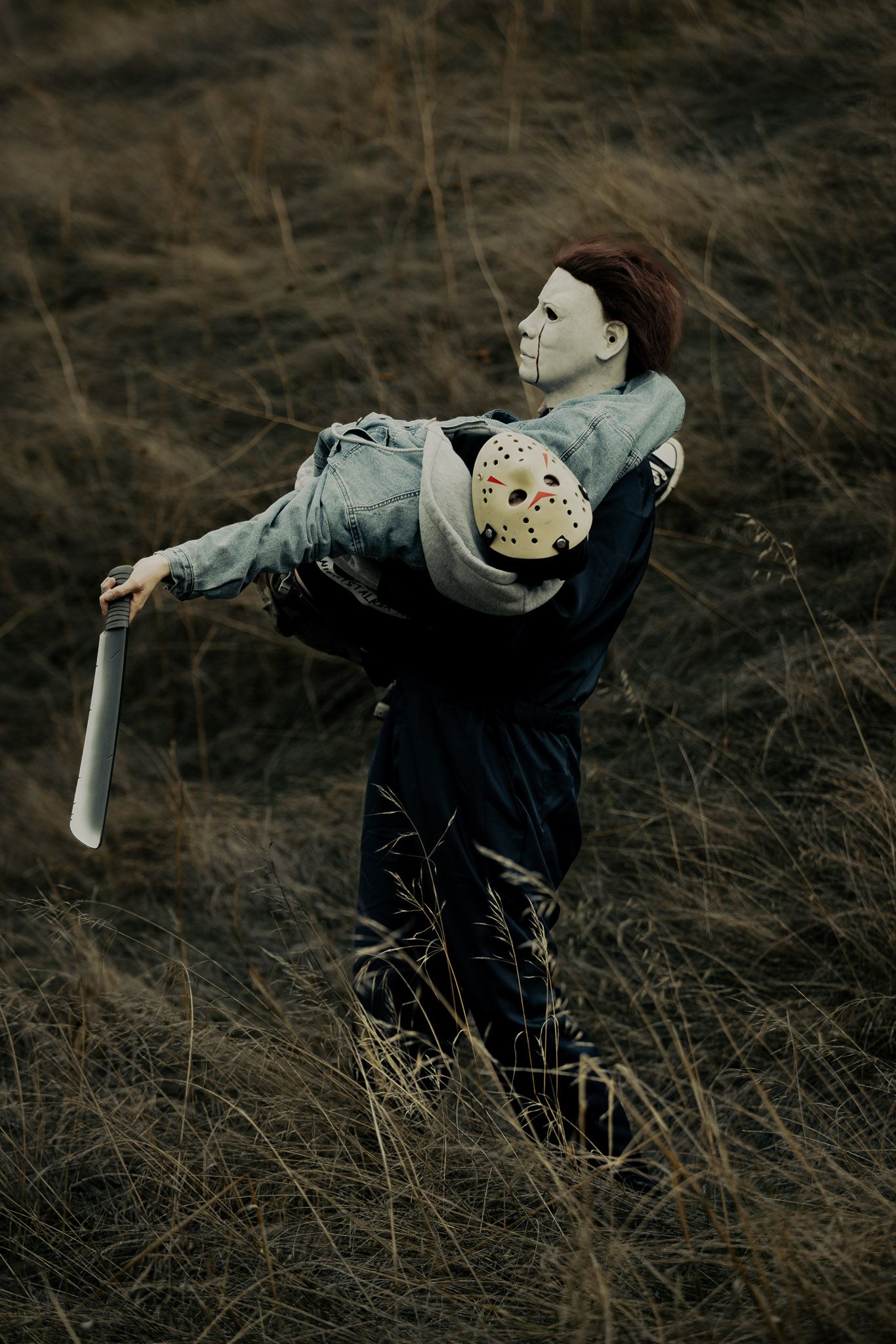 A person in dark clothing spins with outstretched arms in a field of dried grass at dusk.