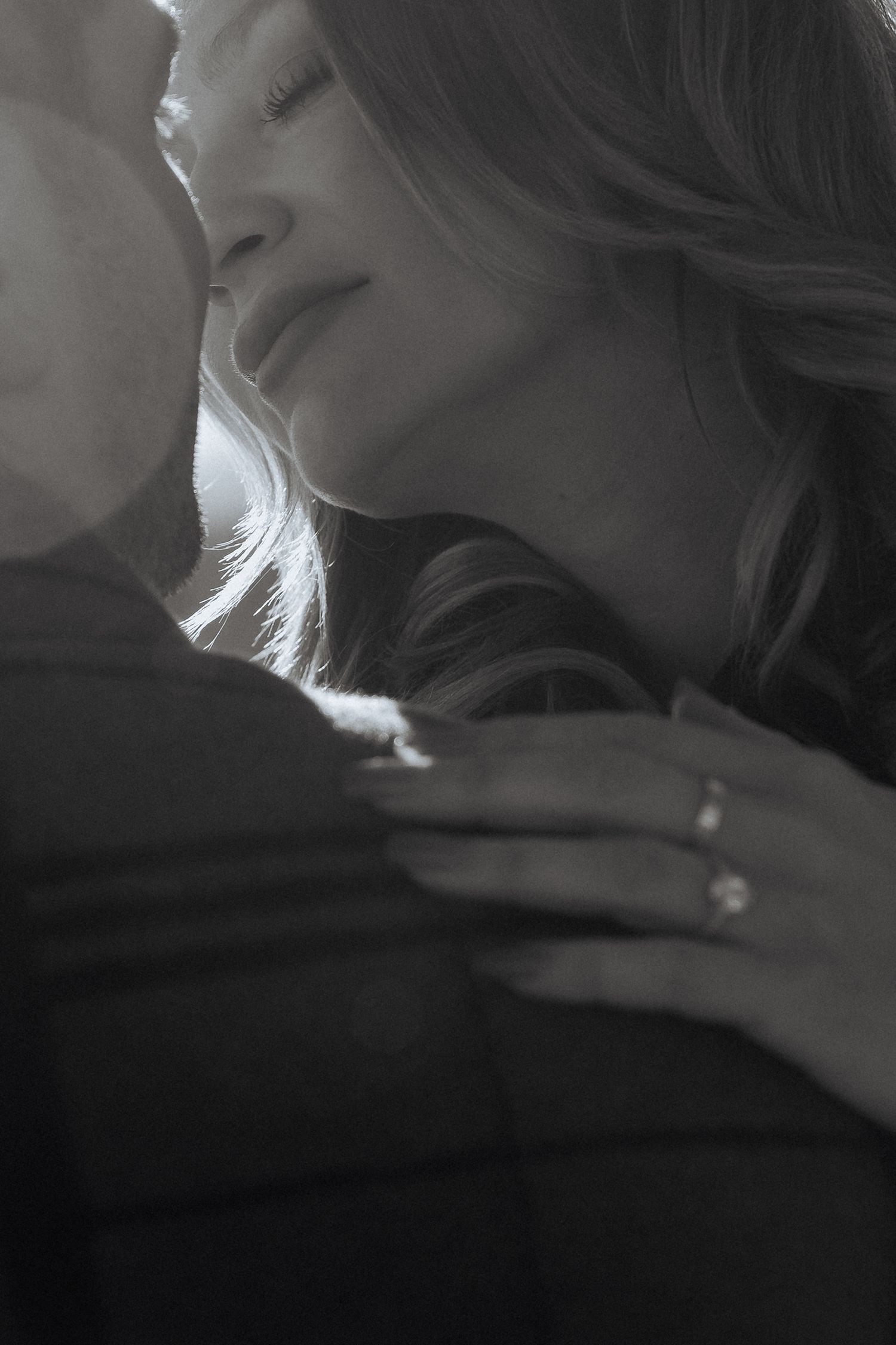 A romantic black and white close-up photograph showing an intimate embrace with soft lighting and flowing hair.