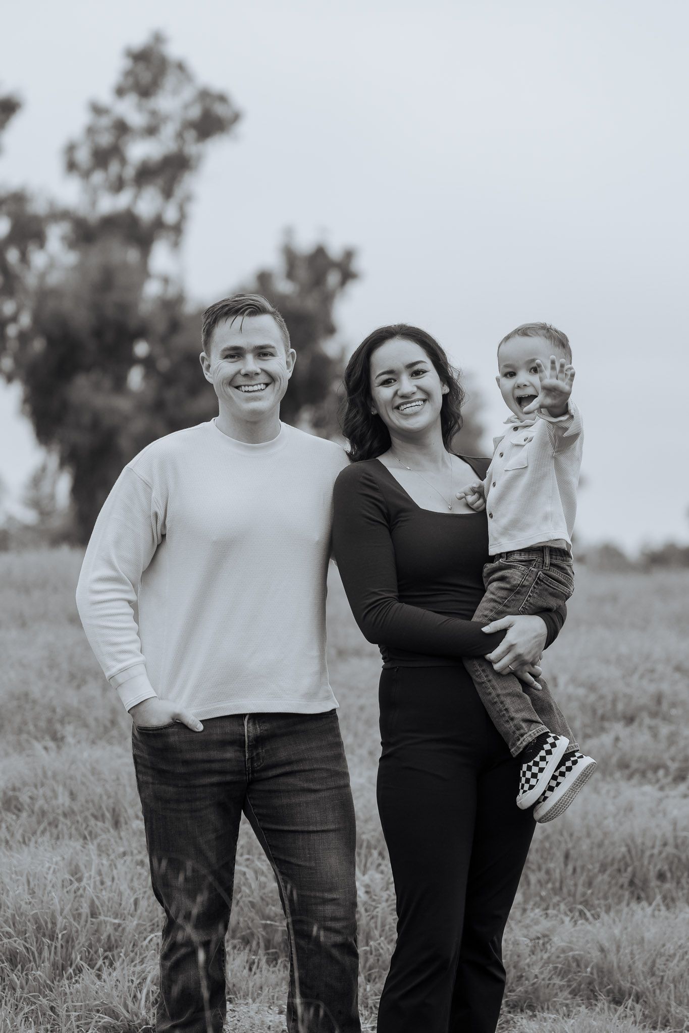 Family of three poses together in casual outfits during an outdoor black and white photo session.