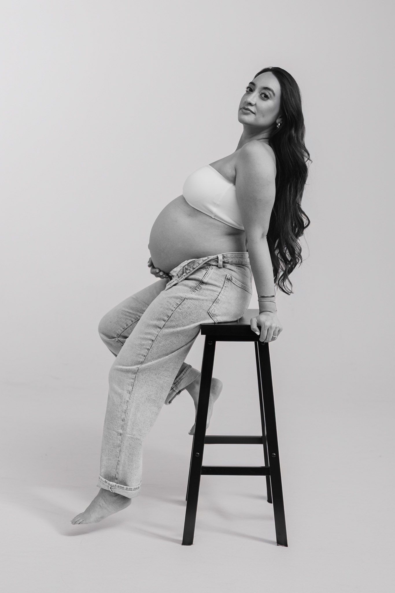 Artistic black and white maternity photos with woman posing on stool in studio setting.
