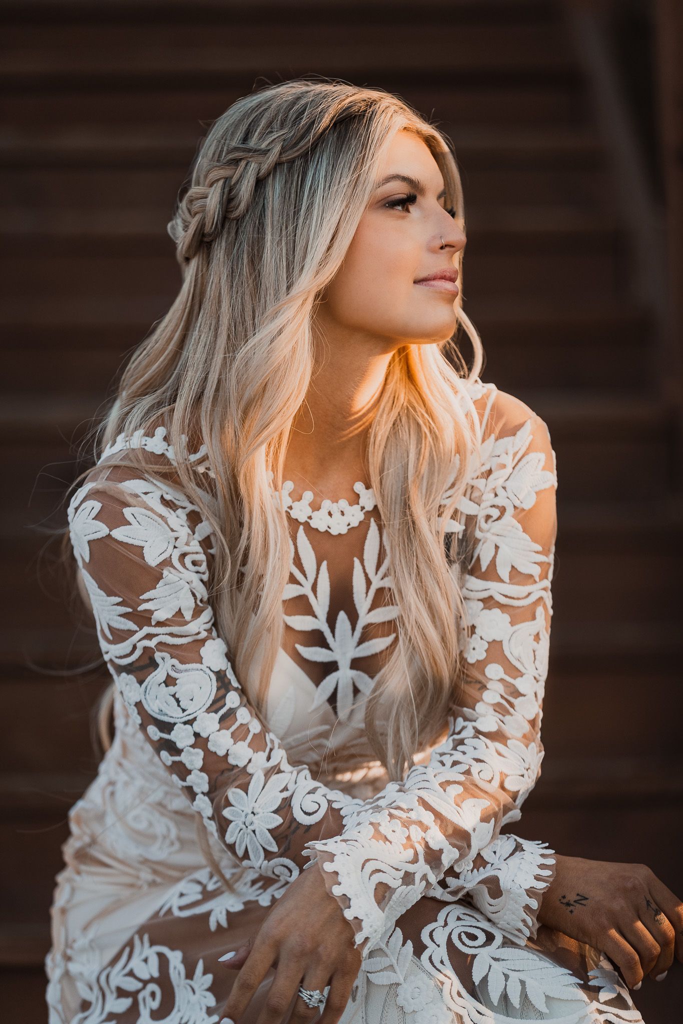 Bride in detailed lace gown with braided hair poses in golden sunlight.