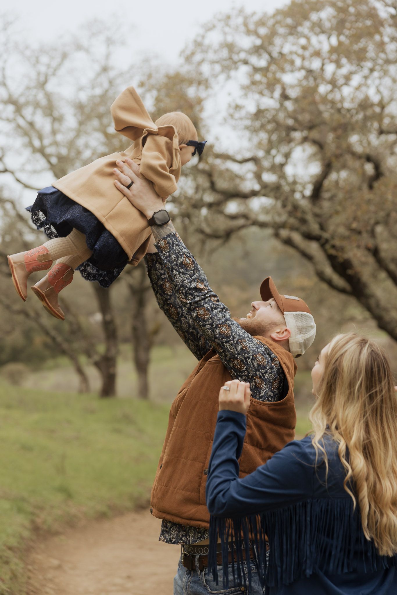 Parent lifts child wearing tan coat in joyful outdoor play sequence.