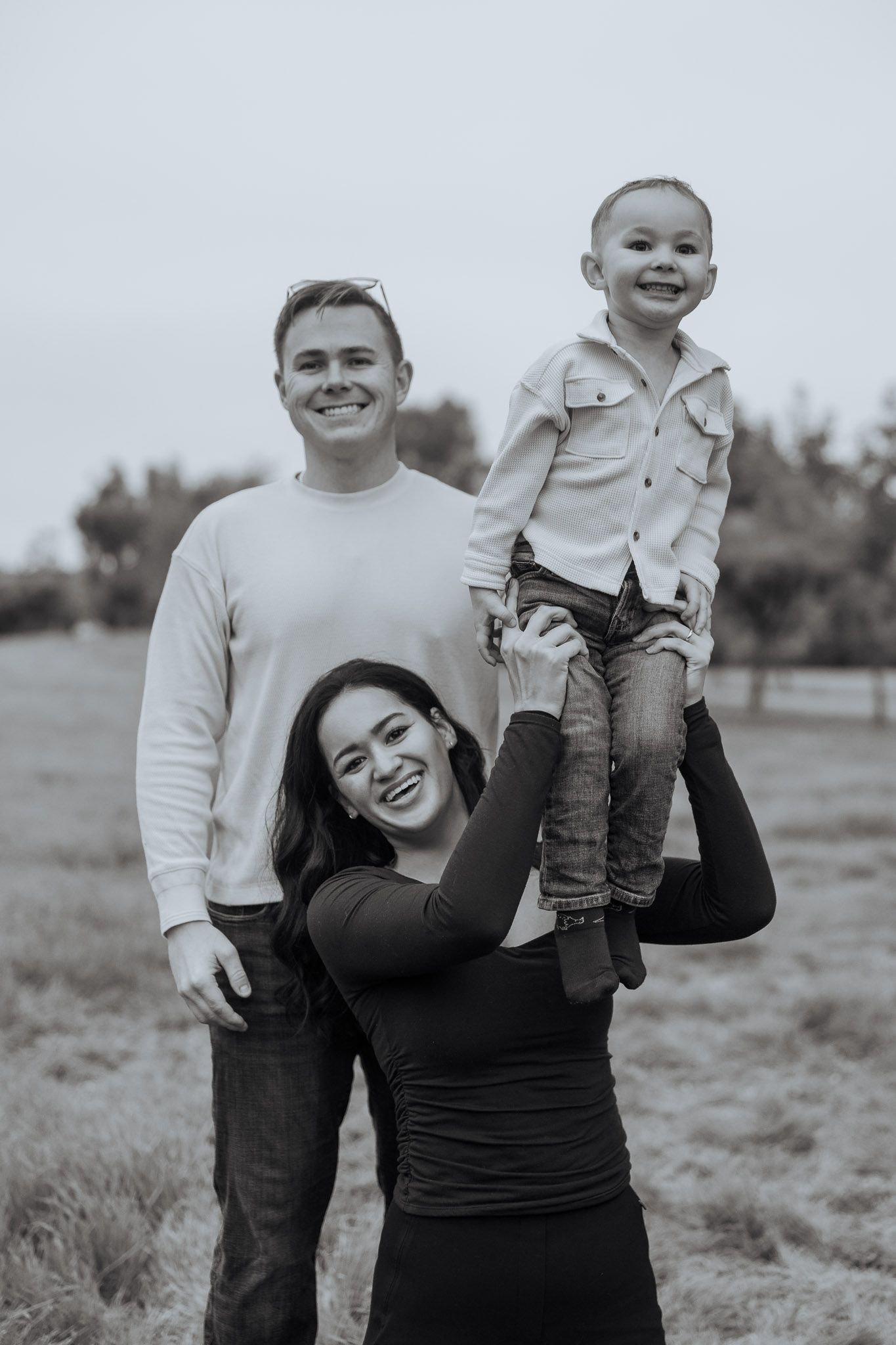 A joyful black and white outdoor portrait series showing playful interactions between parent and child in a field.
