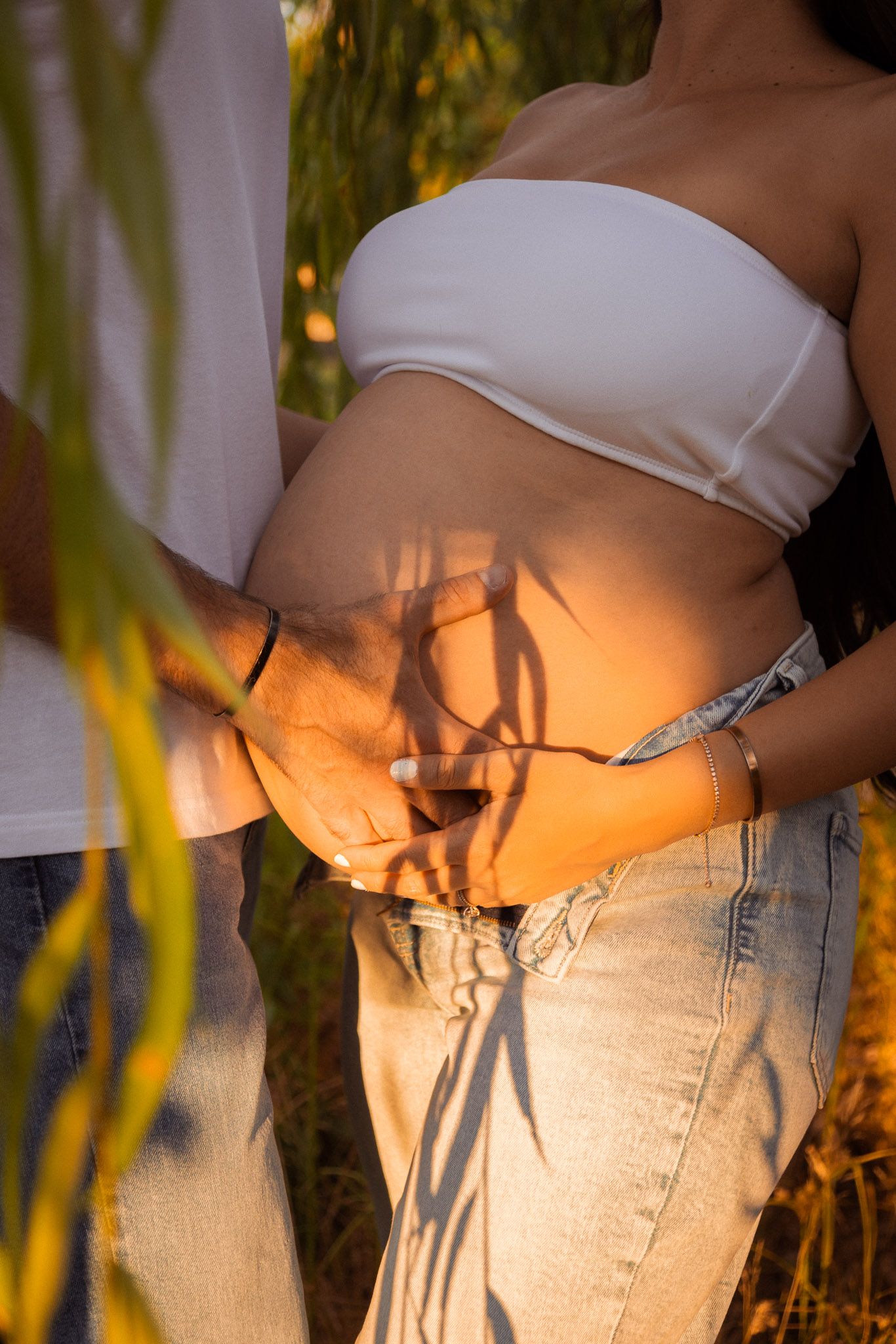 Person wearing white crop top and light wash jeans poses against sunset lighting with palm tree shadows.