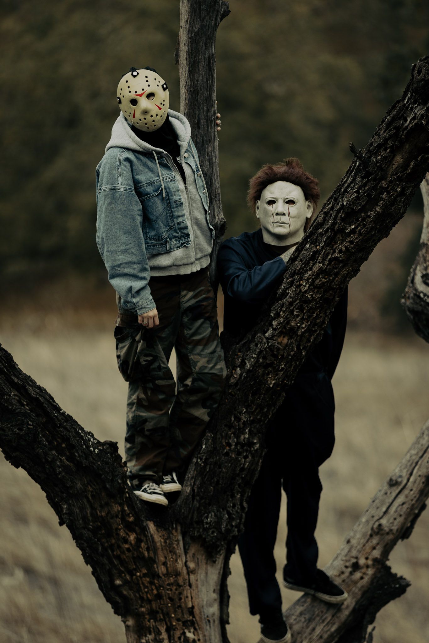 Dark atmospheric photos showing figures in horror masks posed against a gnarled tree trunk.