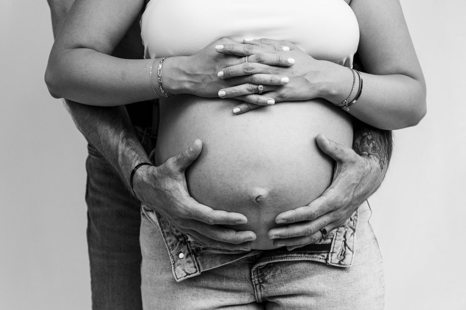 Black and white photo series showing a person's hands cradling and revealing their pregnant belly at different stages.