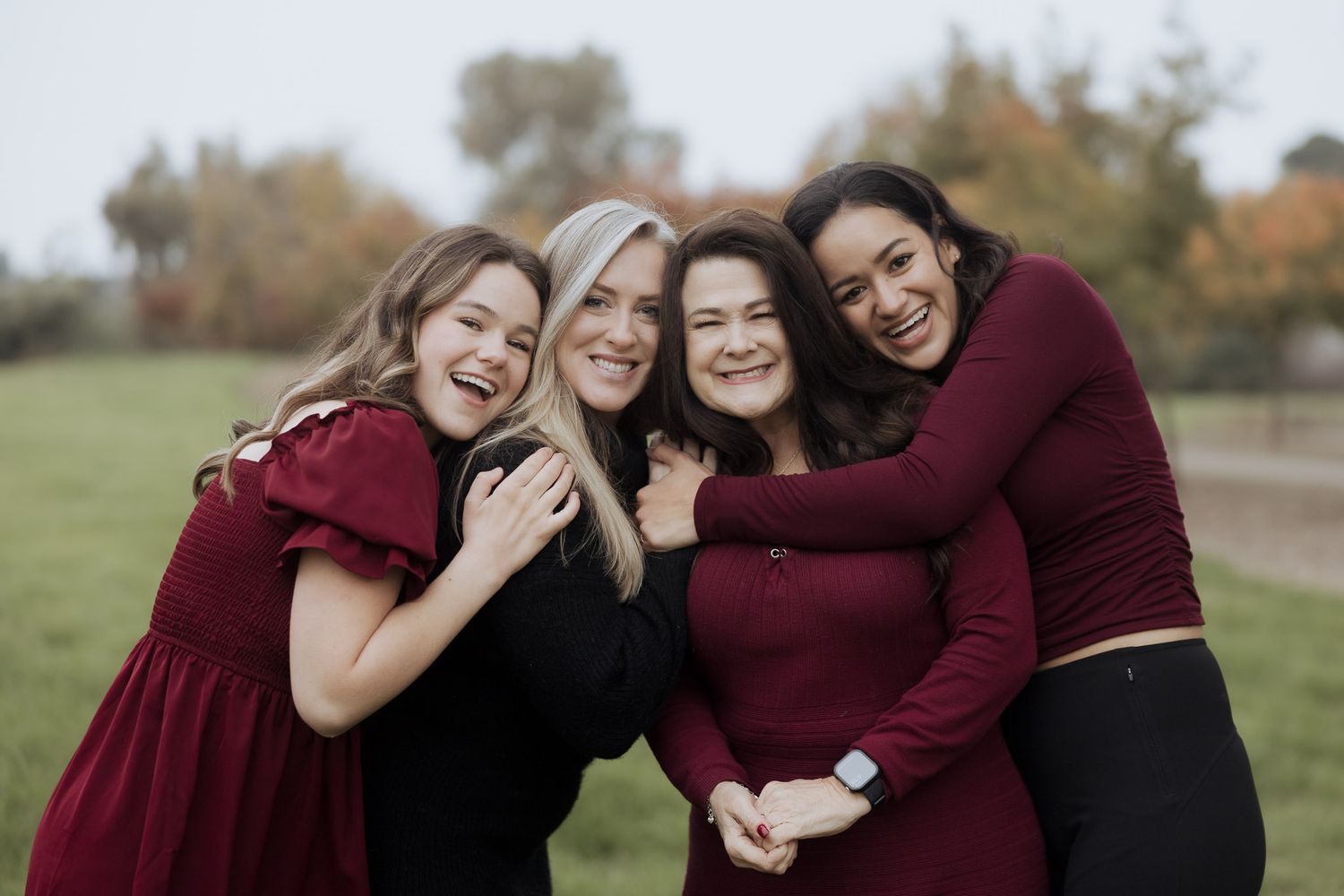 Family group wearing burgundy and black poses together outdoors during autumn.