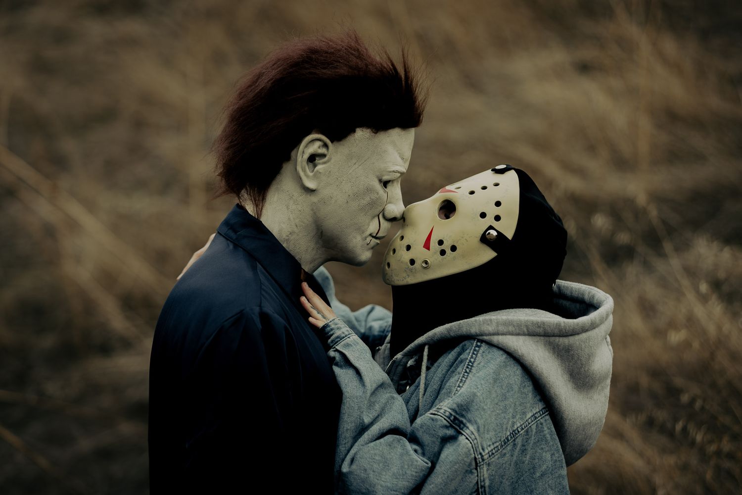 Intimate moment between two people with one wearing a white hockey mask against a dark background.