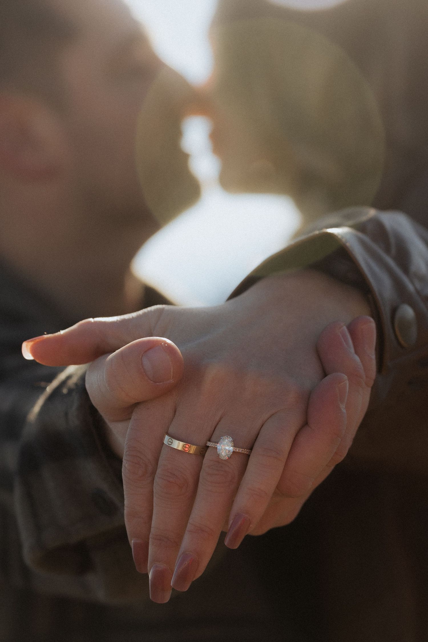 Close-up of an engagement ring on a hand with sunlight creating lens flare in the background.
