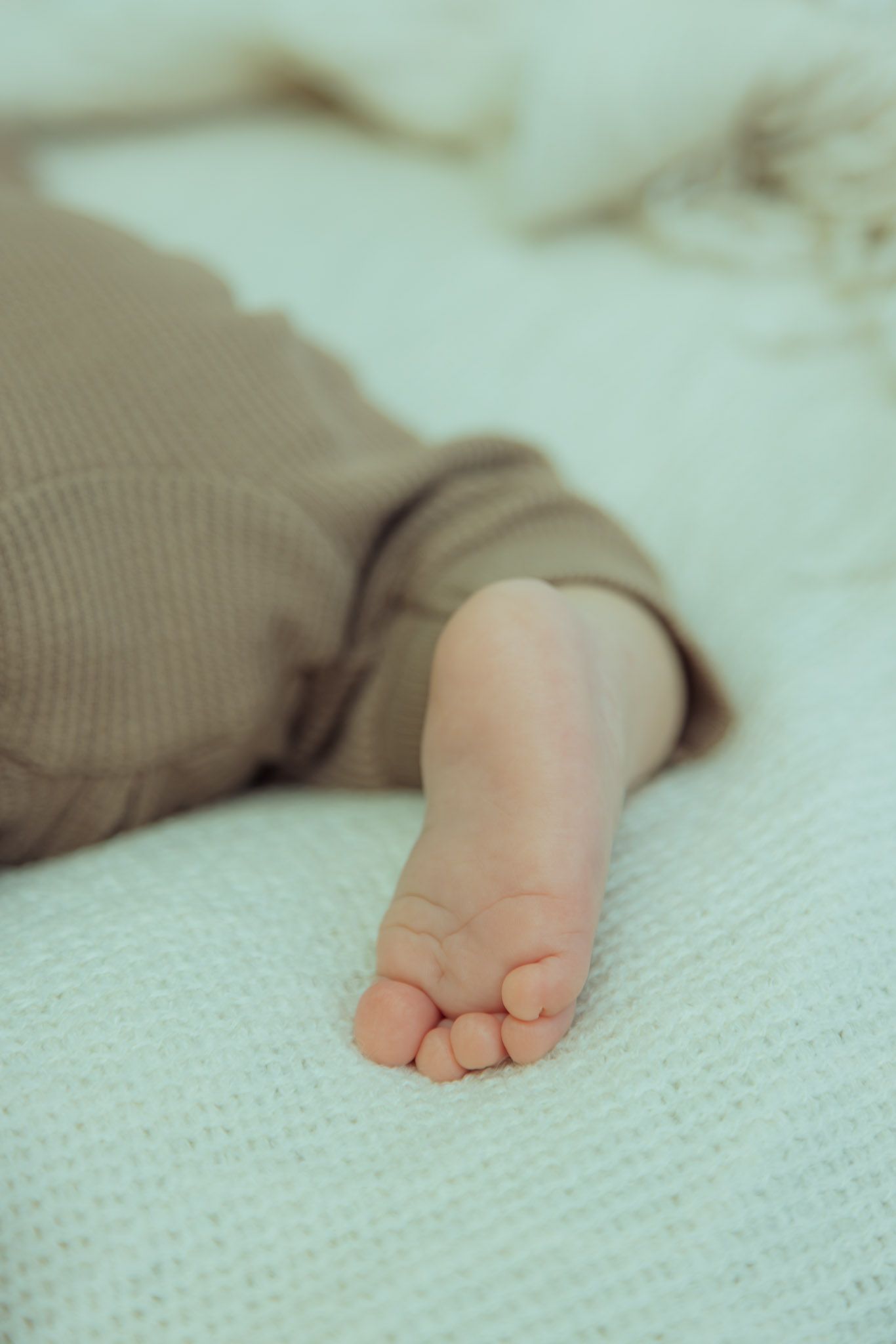 A tiny baby foot rests on soft white knitted fabric, showing delicate toes and smooth skin.