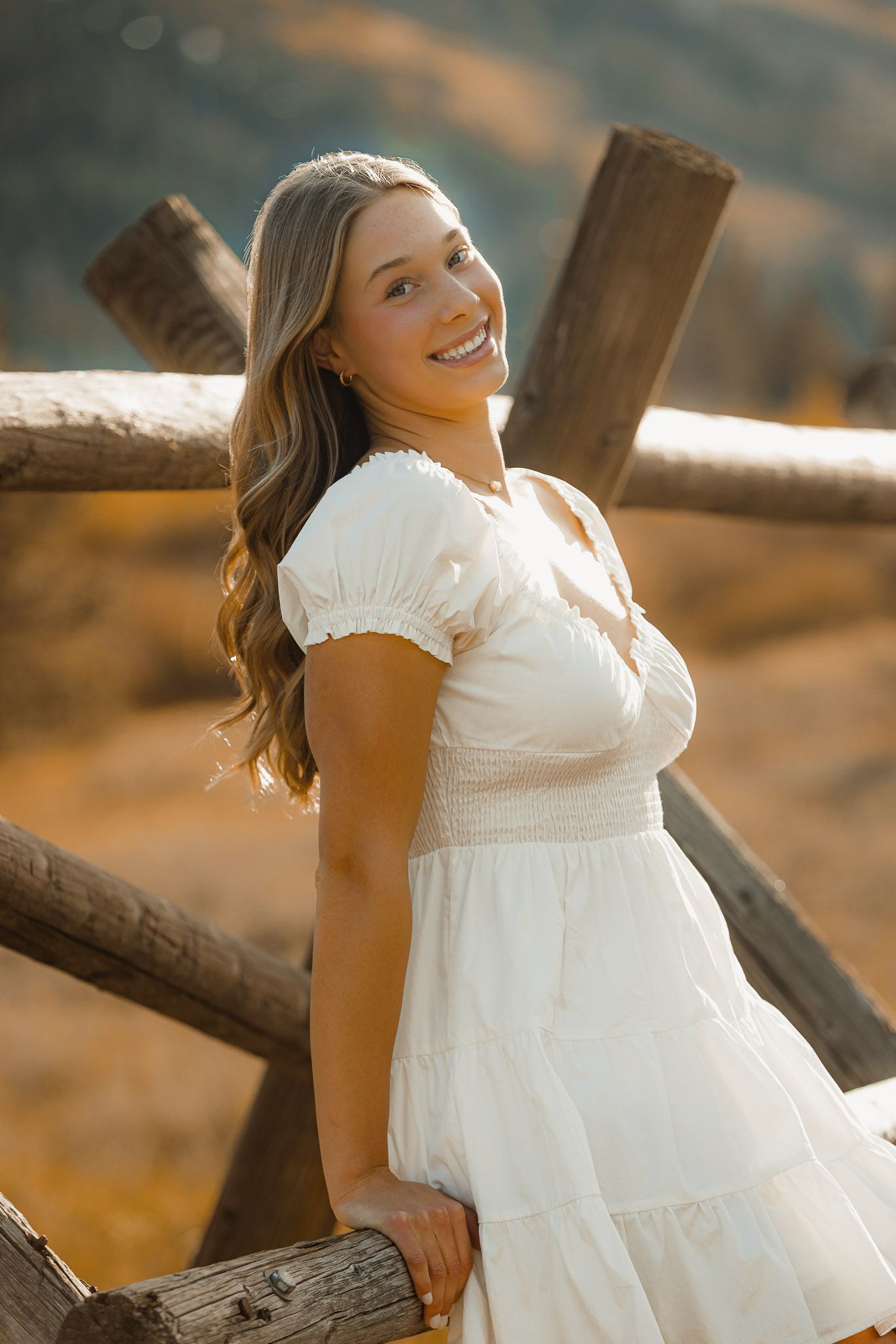 A white dress photoshoot at sunset features poses against a rustic wooden fence in warm golden light.