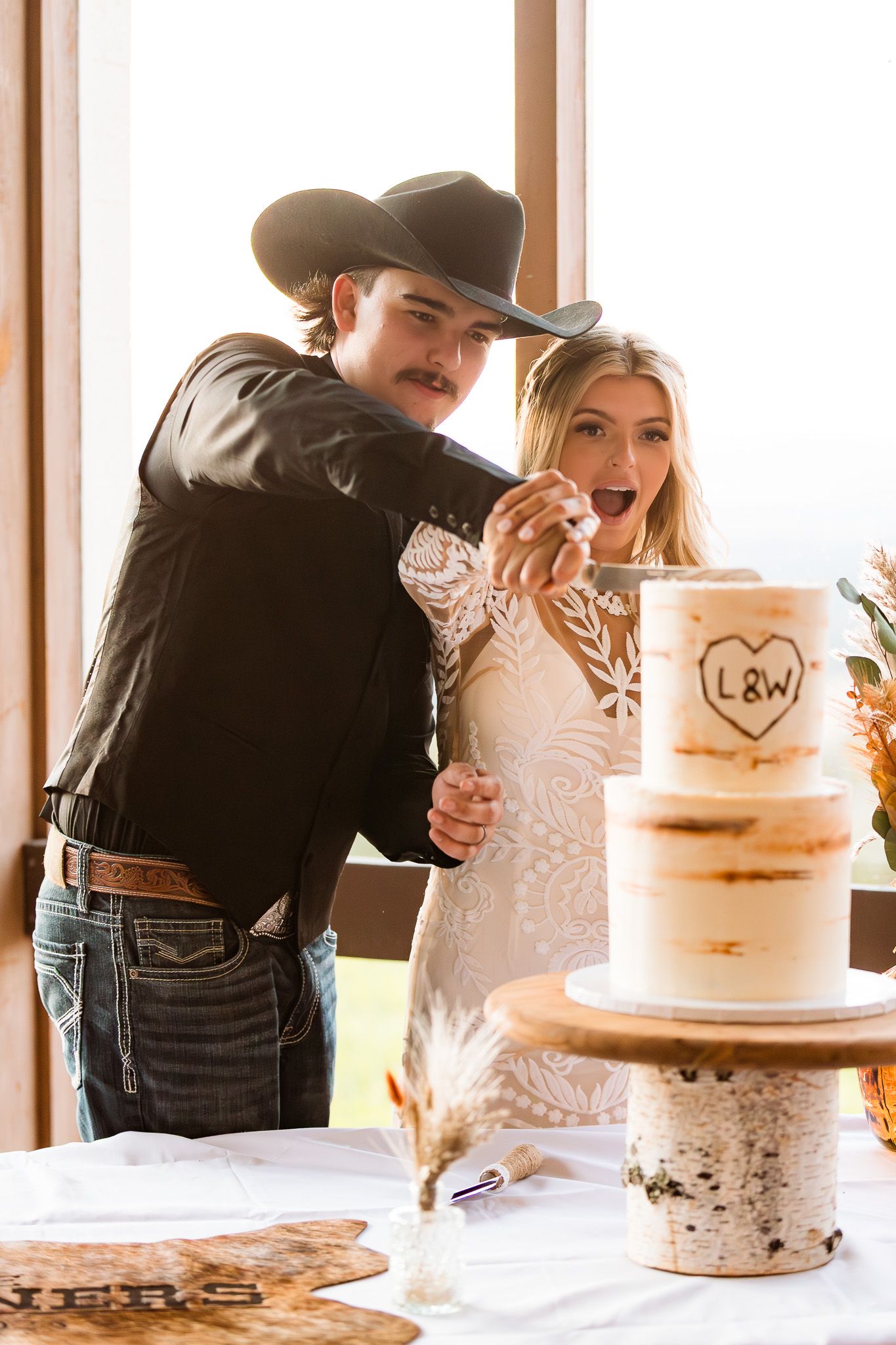 Couple feeds each other wedding cake decorated with initials and rustic details.
