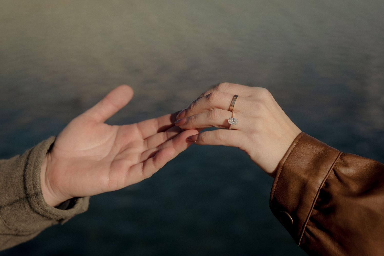 Two hands reaching towards each other against a dark background in a tender gesture.