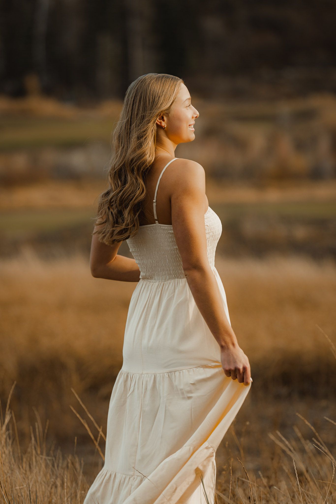 Candid portrait session in a golden field shows movement and joy at sunset with mountains in background.