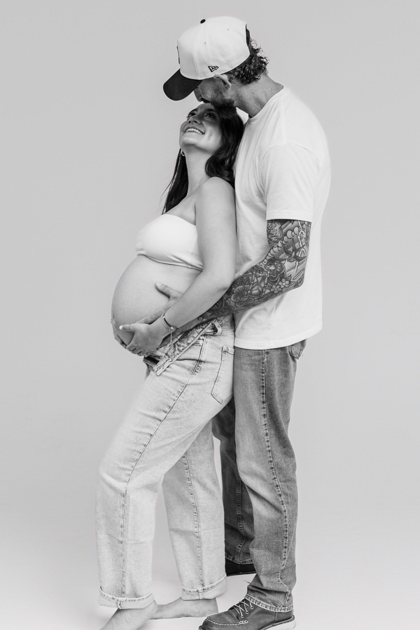 Minimalist black and white maternity photos showing couple embracing against plain background.